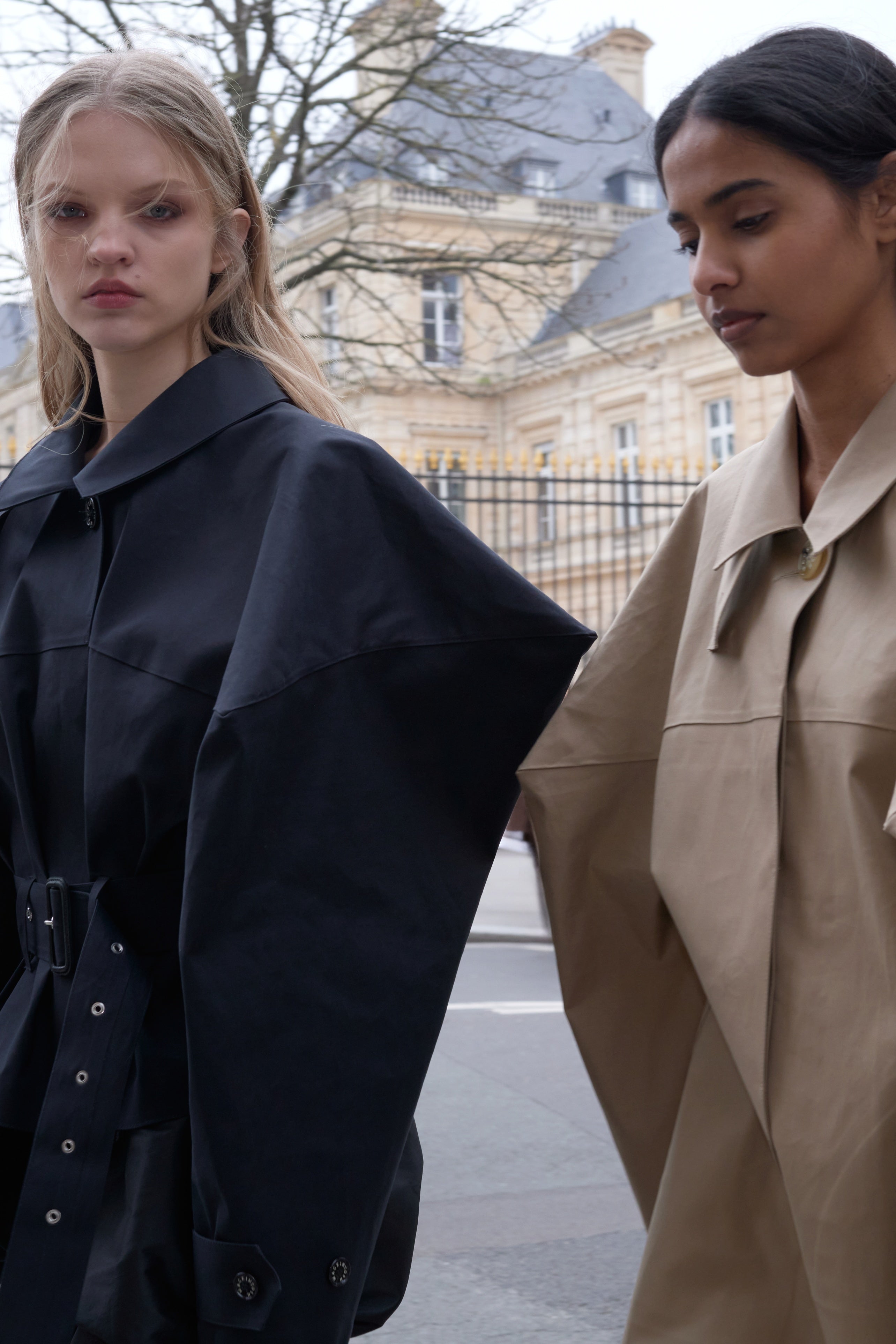 Two models standing outside wearing black and beige coats.