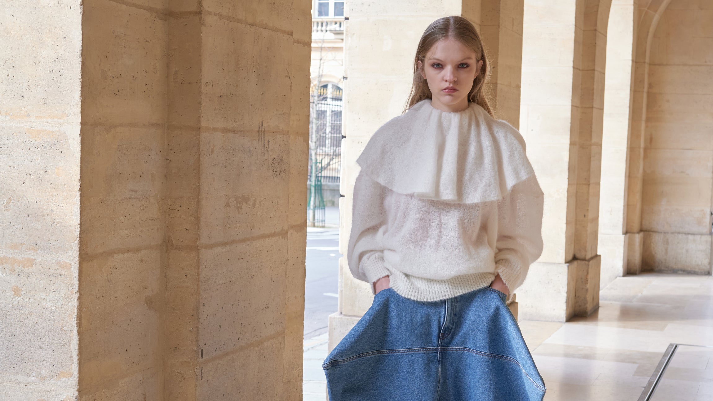 Model wearing a white knit sweater with a volant collar and jeans.