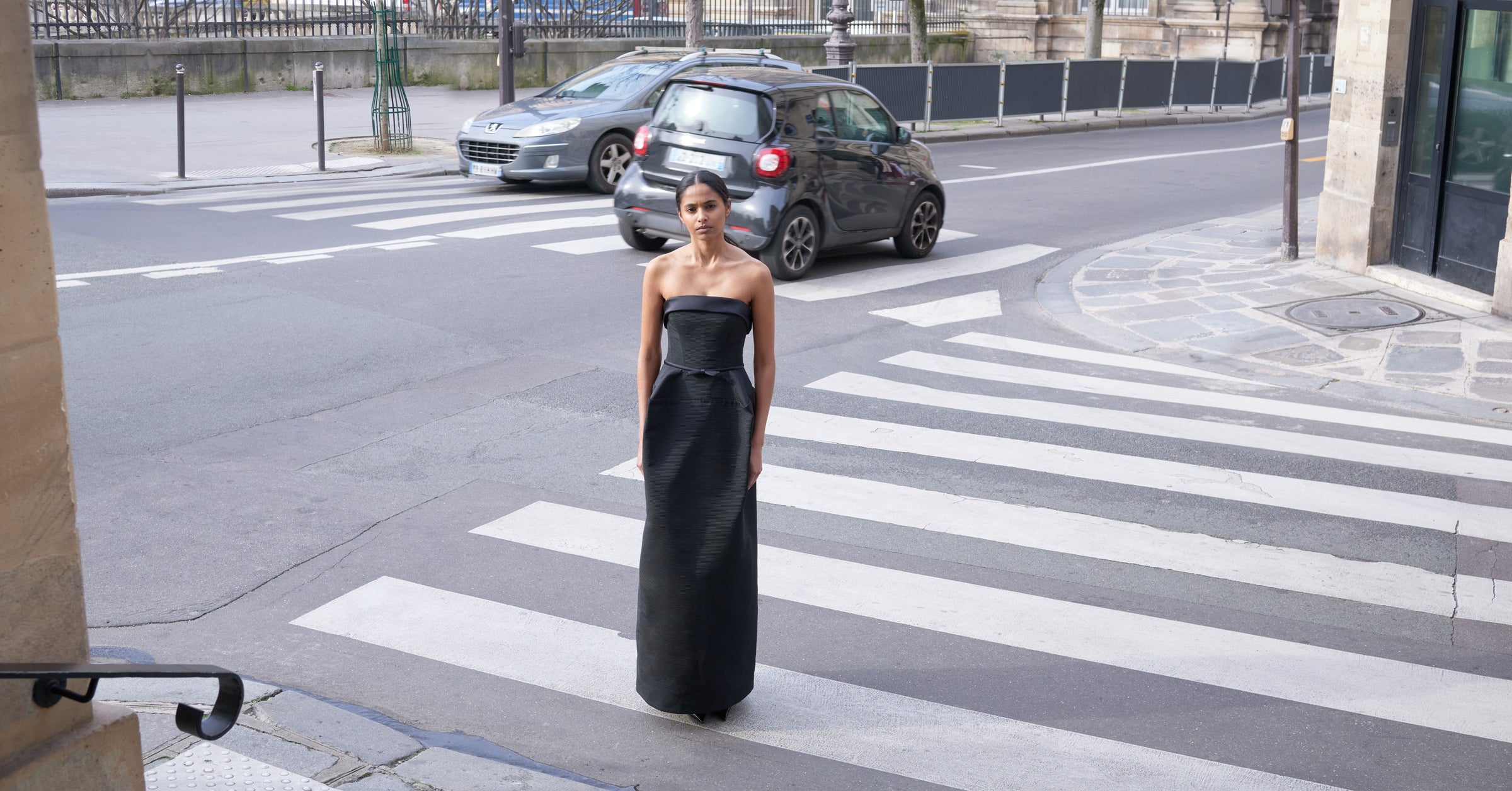 Model wearing a black strapless long dress outside on a street.