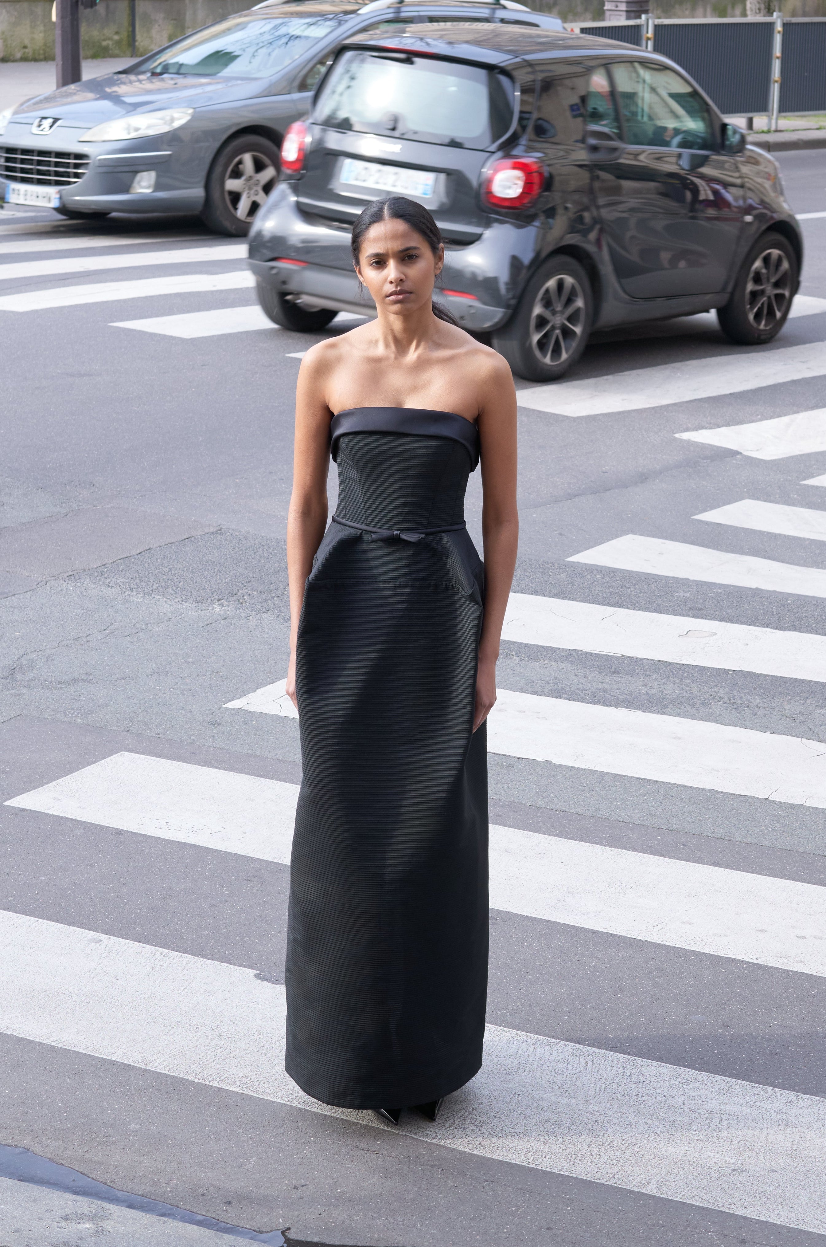 Woman standing in a busy street wearing a black gown.