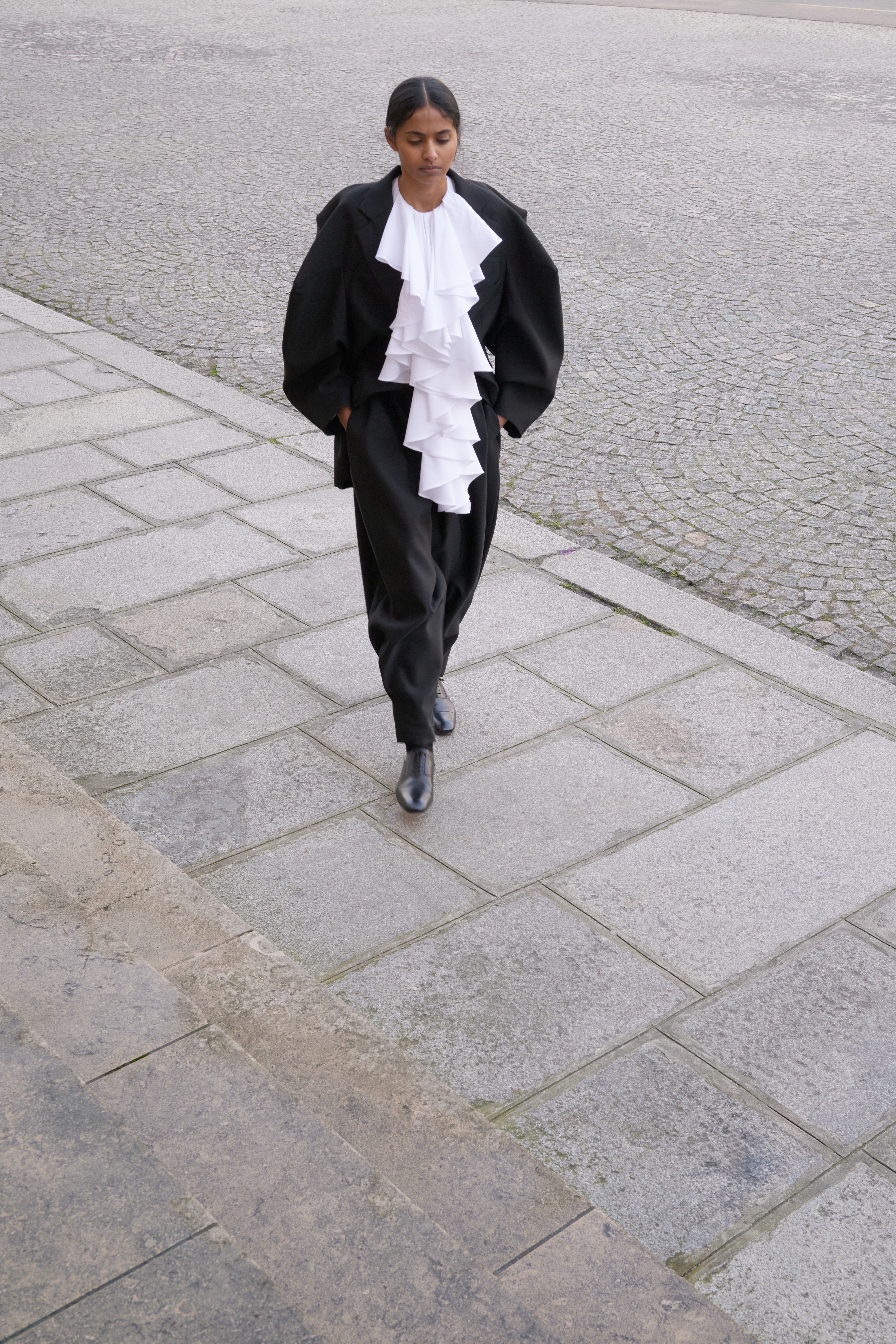 Person walking on a paved street wearing a black outfit with a white shirt.