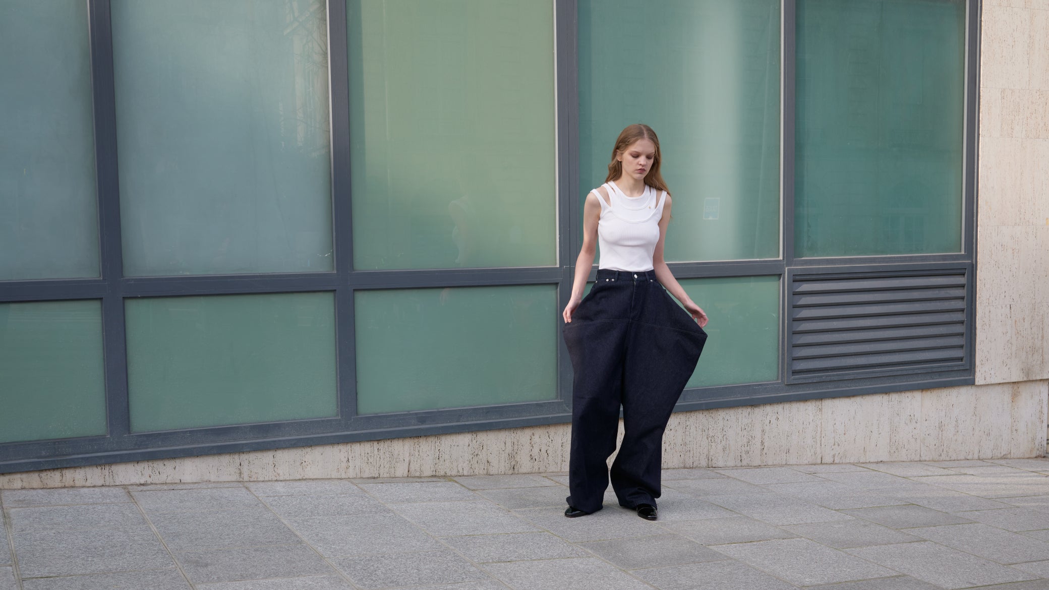 Woman wearing a white top and jeans standing in front of a building with large windows