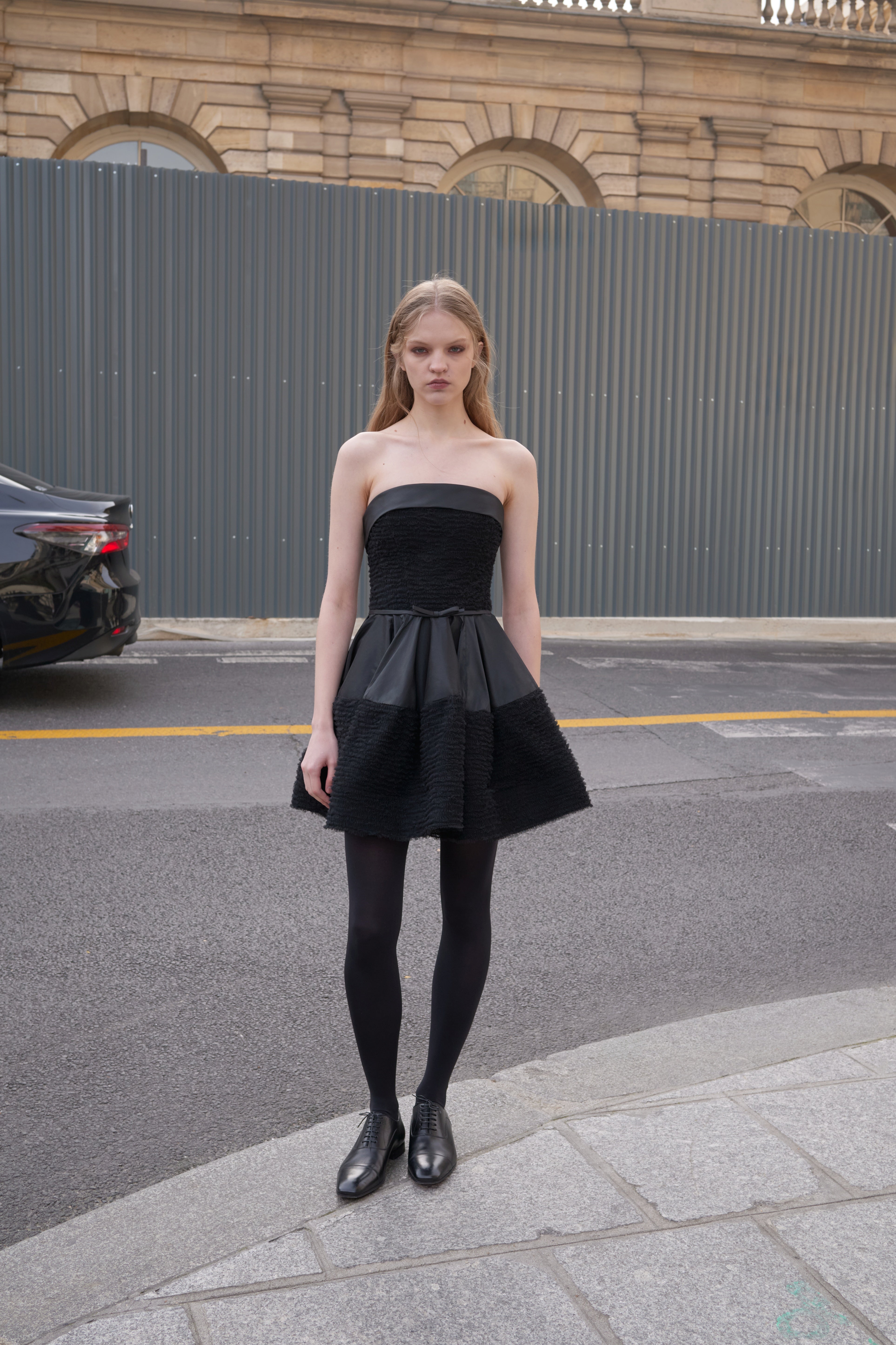 Mode wearing a black strapless dress standing on a pavement.
