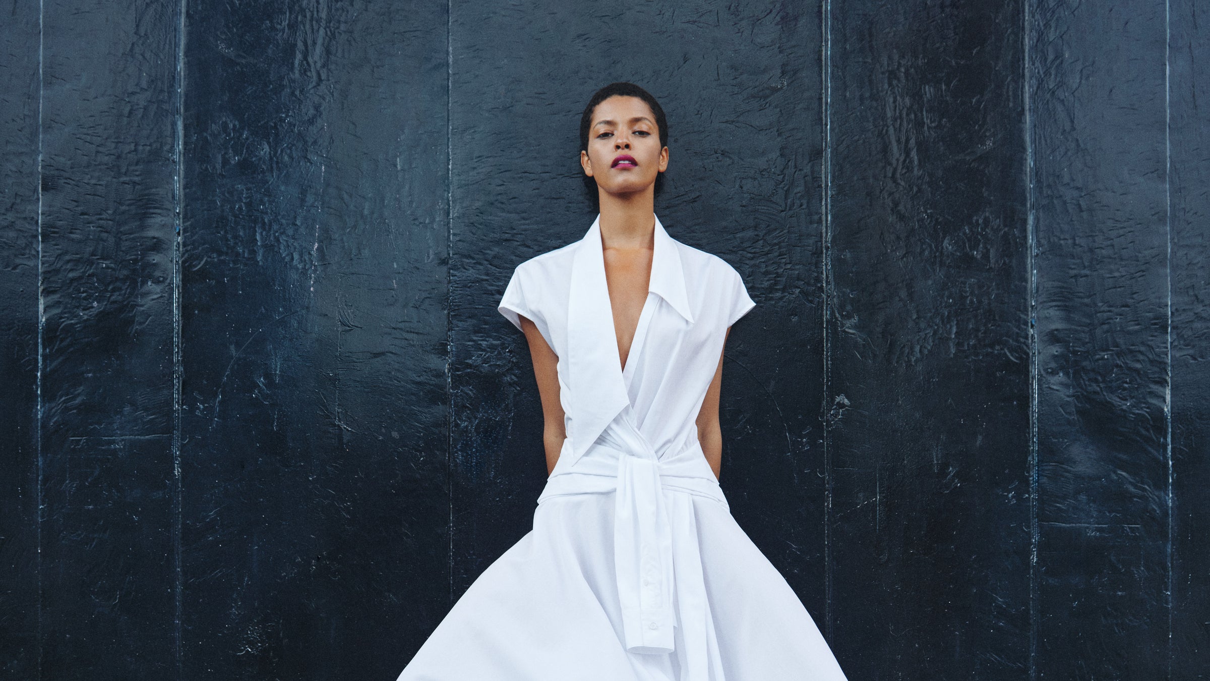 Woman in a white dress standing against a dark textured wall