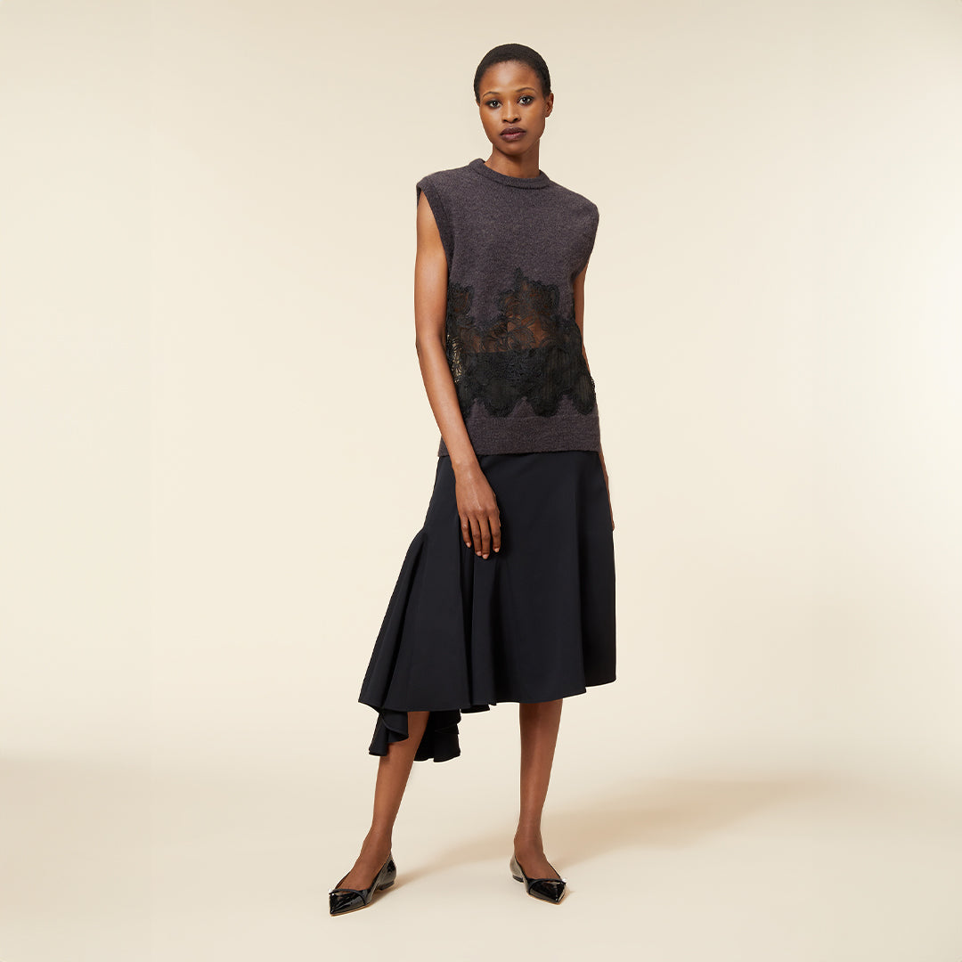 The model wears a sleeveless charcoal gray top with floral lace overlay and a flowing black asymmetrical skirt.