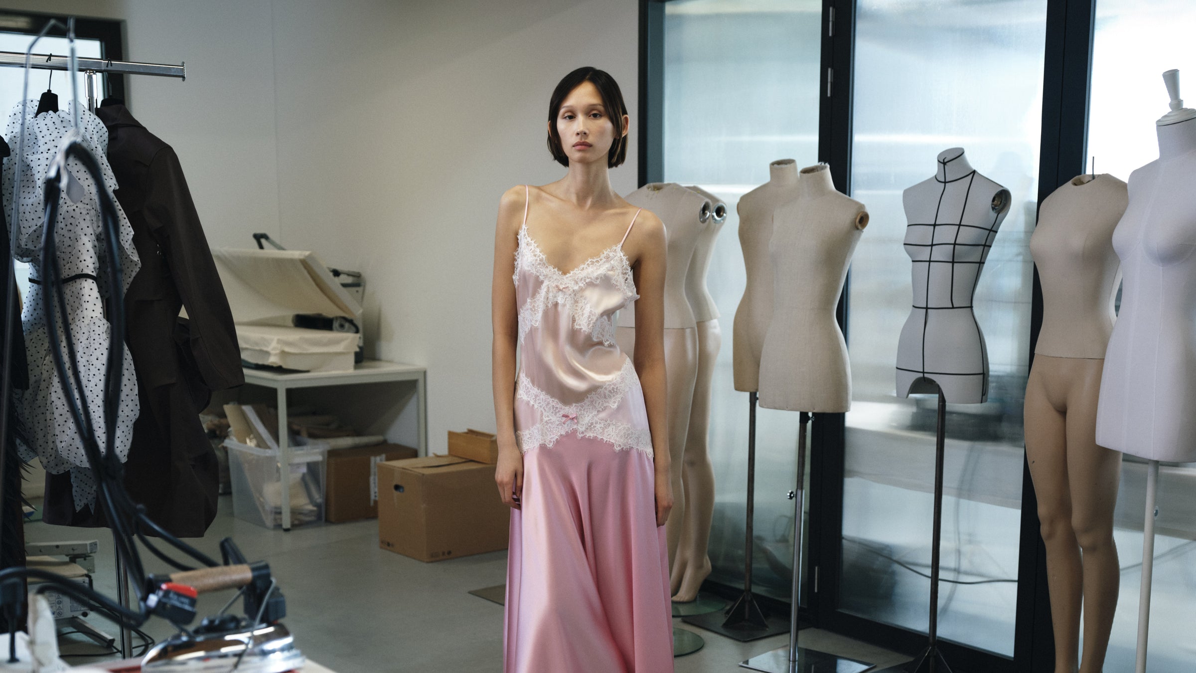 Woman in a pink dress standing in a room with mannequins and fashion design elements.