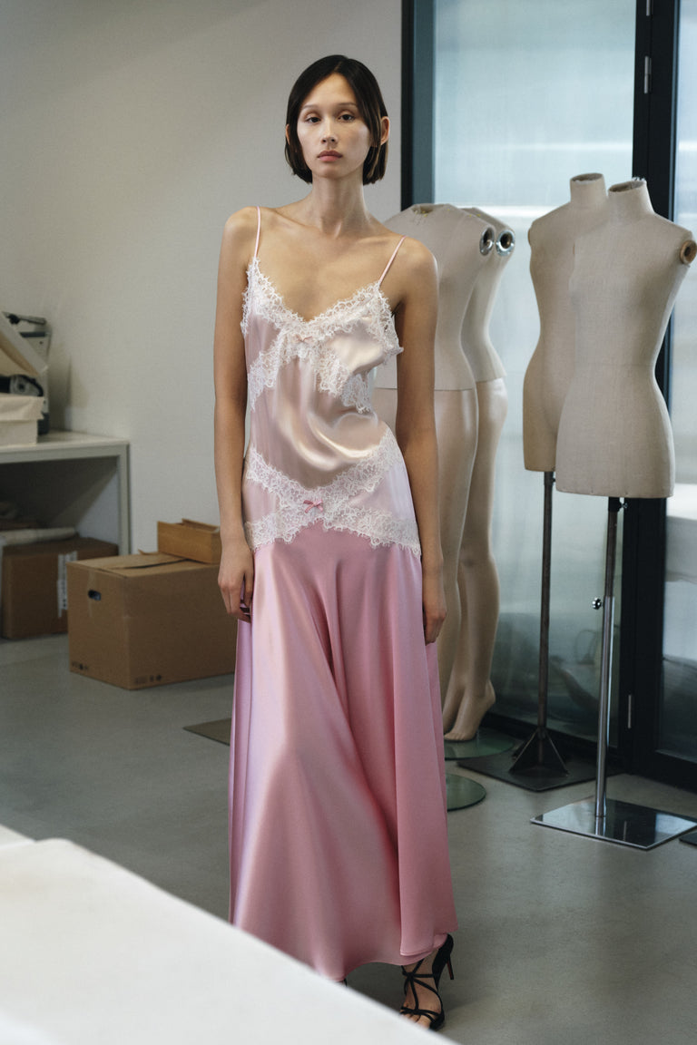 Woman wearing a lace top and pink skirt standing in a room with mannequins and boxes.