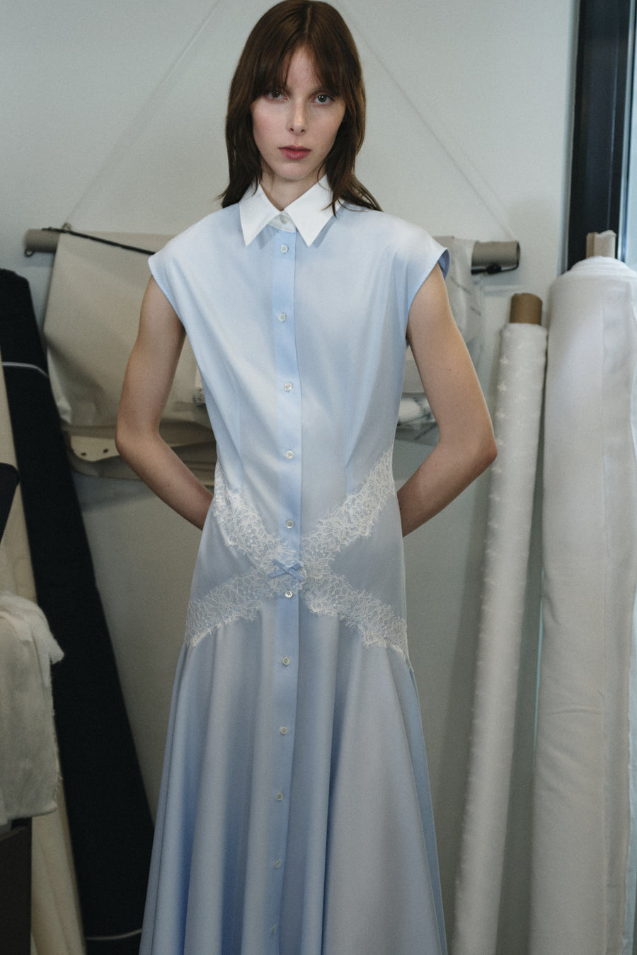 Model wearing a light blue dress with a white collar in a sewing studio.
