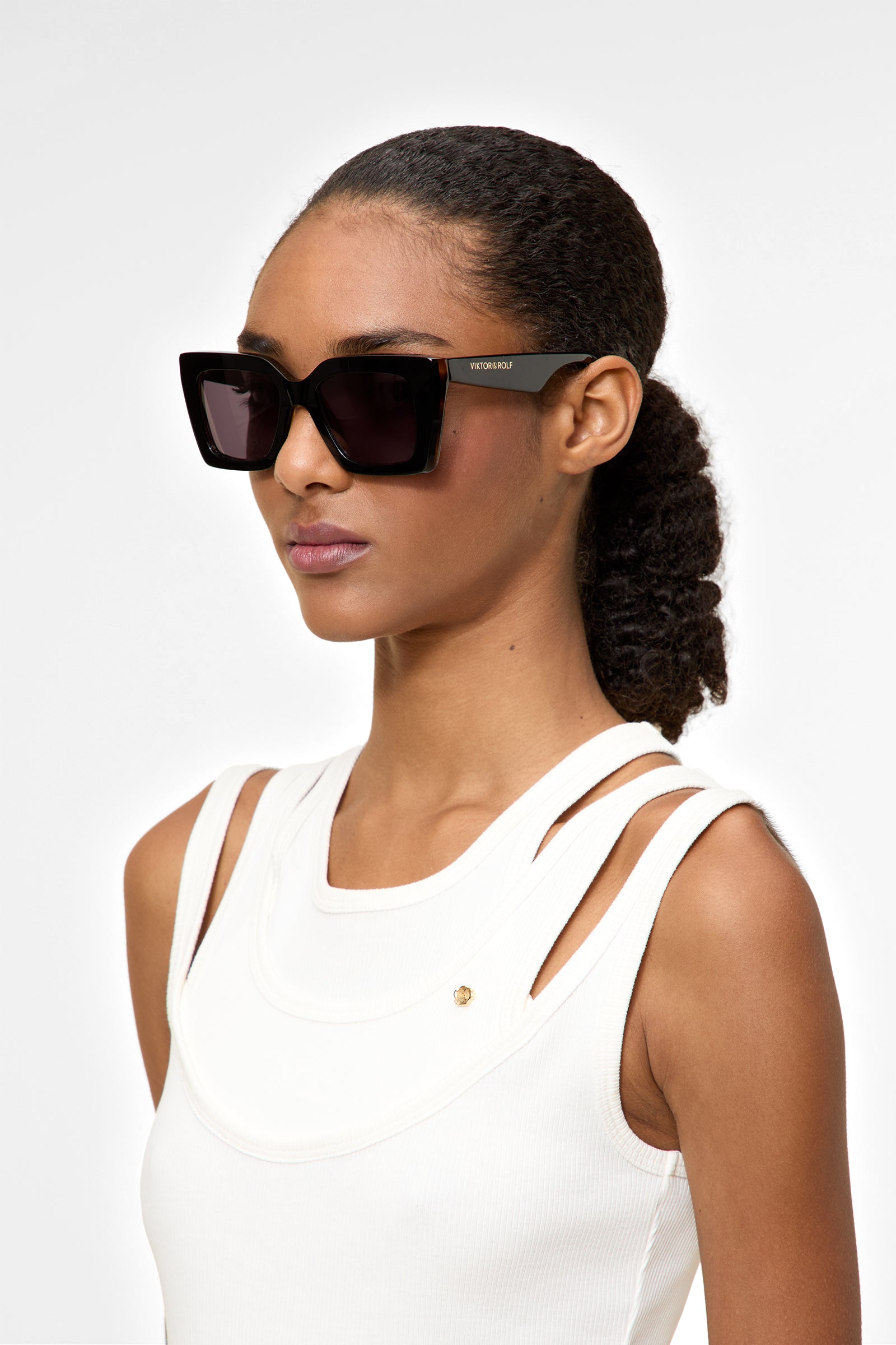 Model wearing black square sunglasses on a white background.
