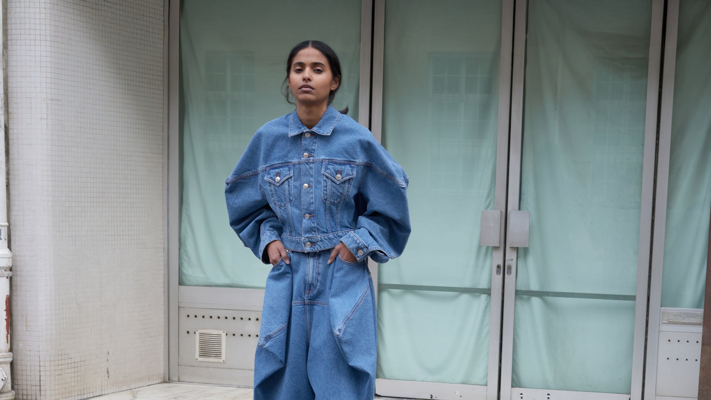 Person wearing a denim outfit standing in front of a glass door.