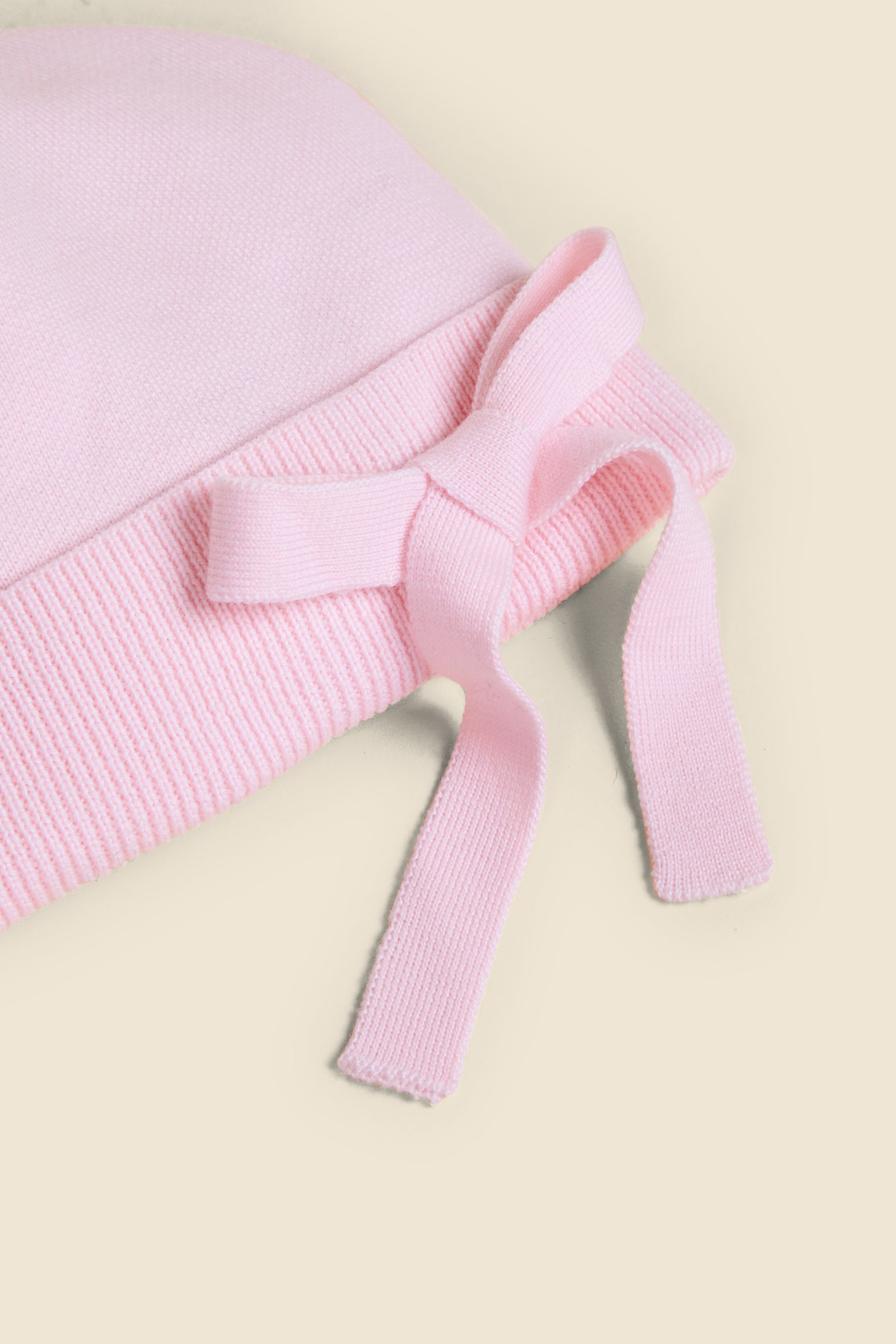 A light pink knit hat with a ribbed texture, featuring a decorative bow detail, crafted from soft, cozy fabric.