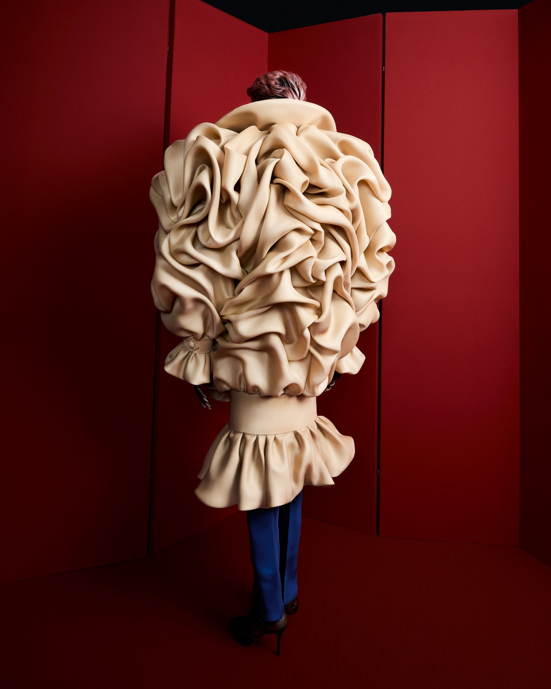 Model wearing a beige haute couture piece on a red background.