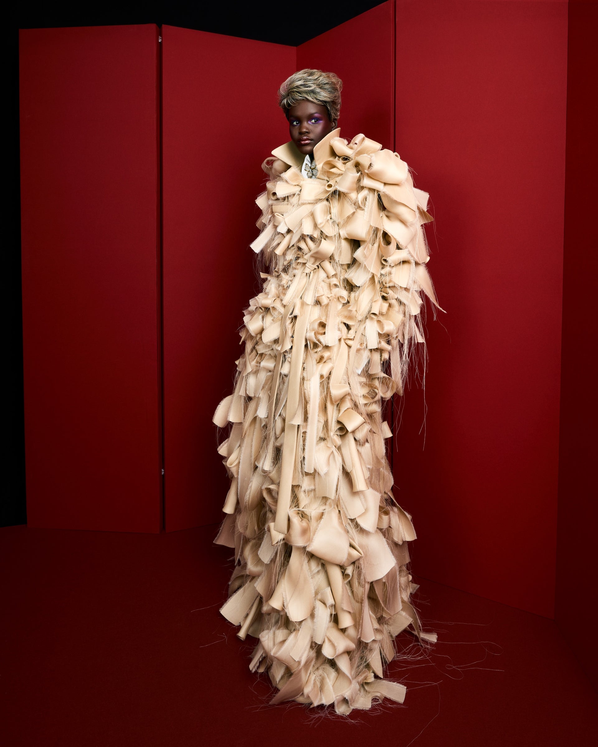 Model wearing a beige haute couture piece on a red background.