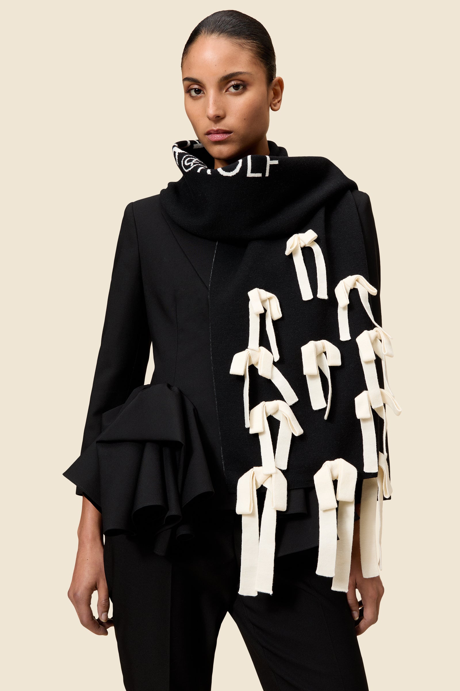 Structured black blazer with dramatic ruffled sleeves paired with a black scarf adorned with white fabric bows.