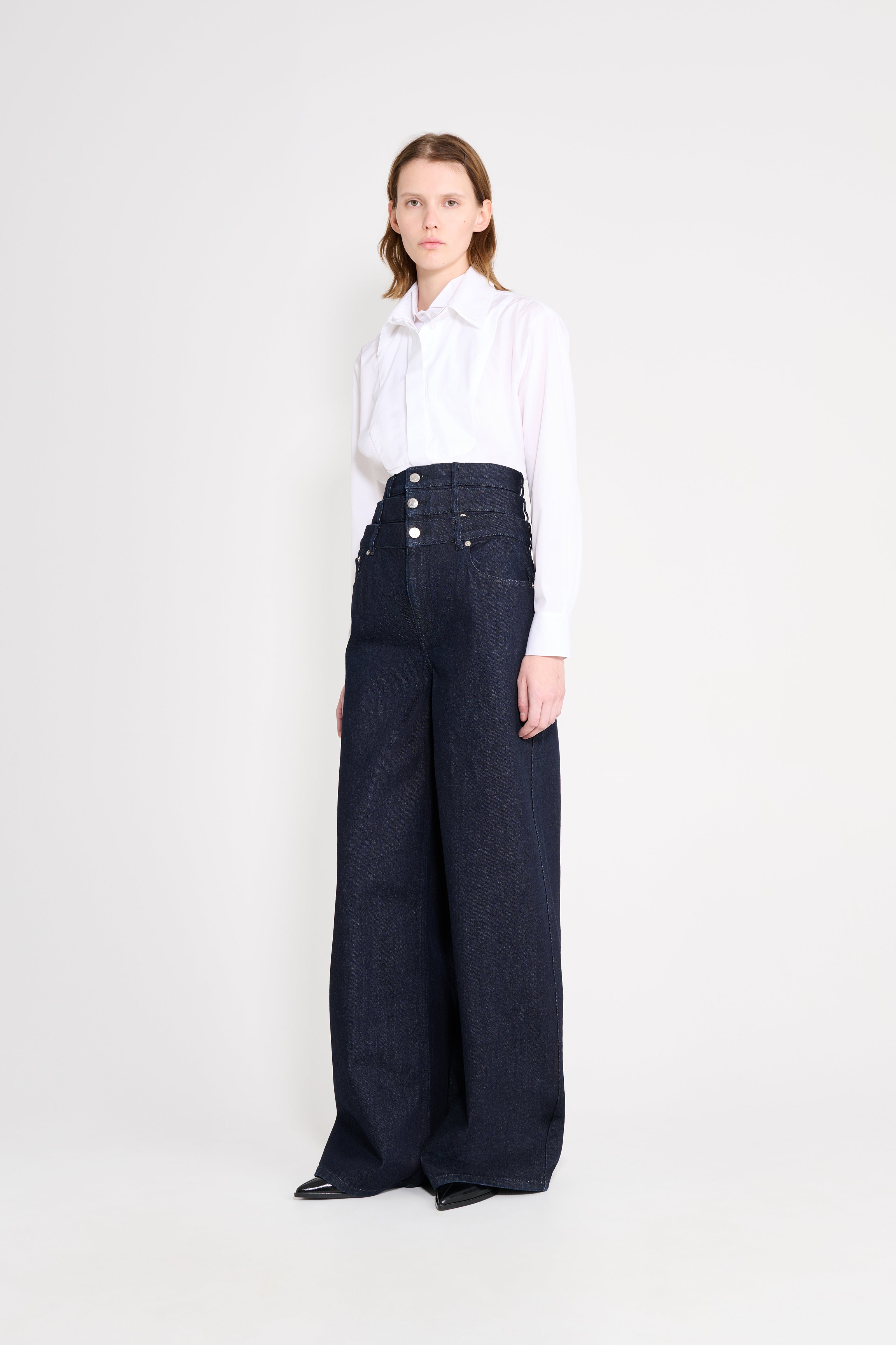 Woman wearing a white blouse and dark blue wide-leg pants on a white background