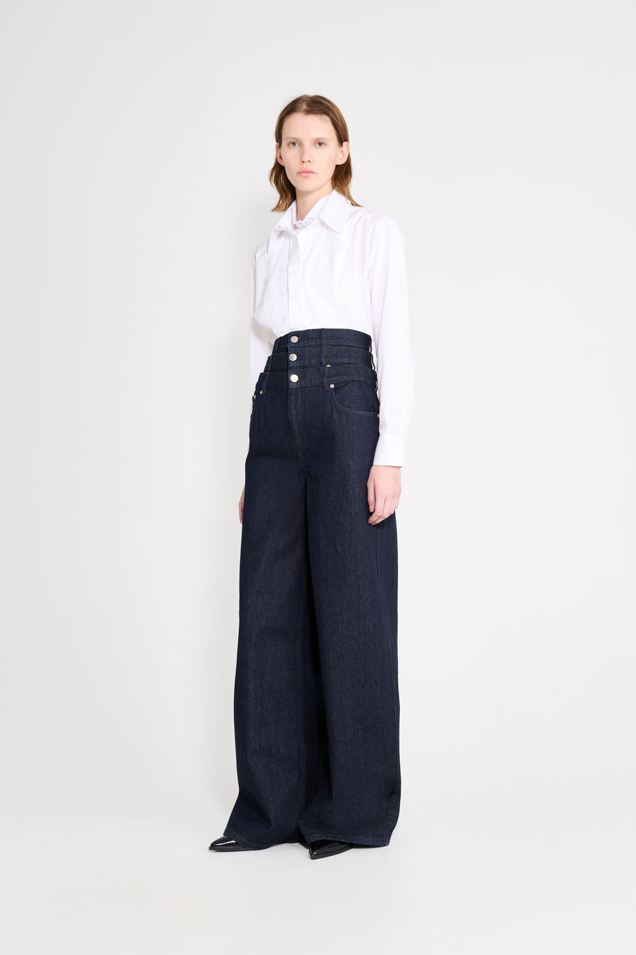 Woman wearing a white blouse and dark blue wide-leg pants on a white background