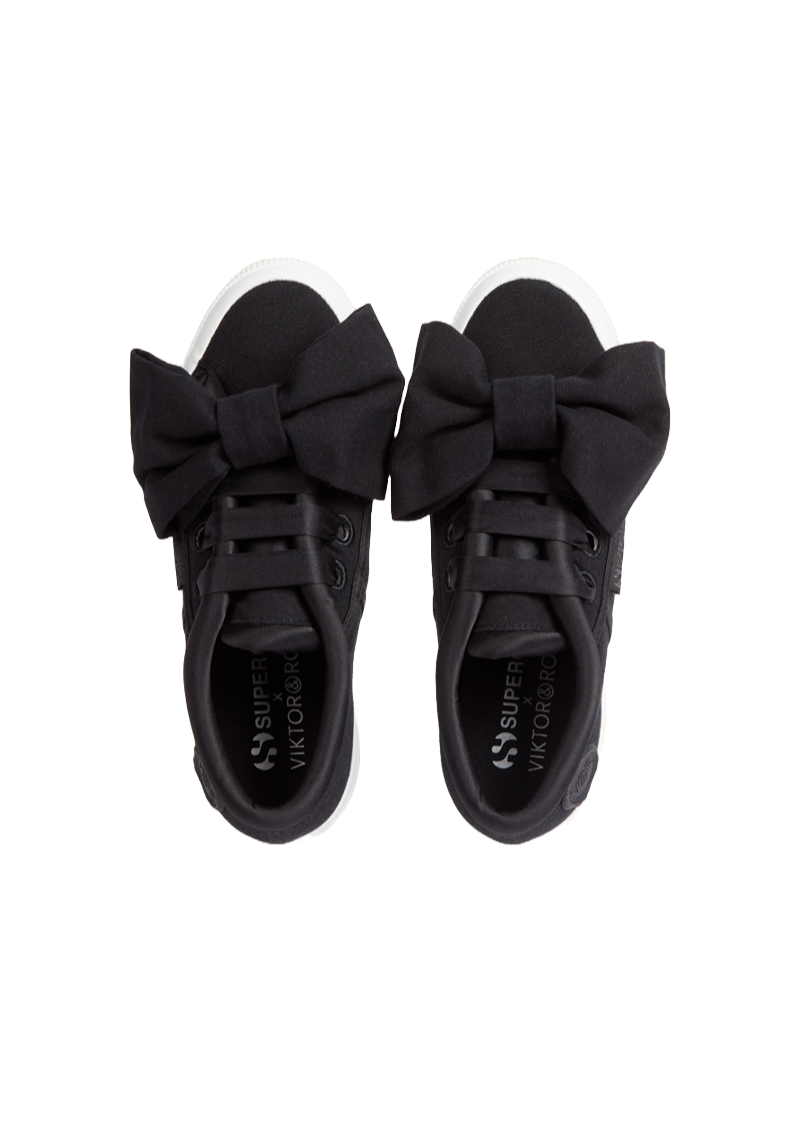 Black sneakers feature oversized fabric bows on the laces, blending playful design with classic style, ideal for fashion-forward wearers.