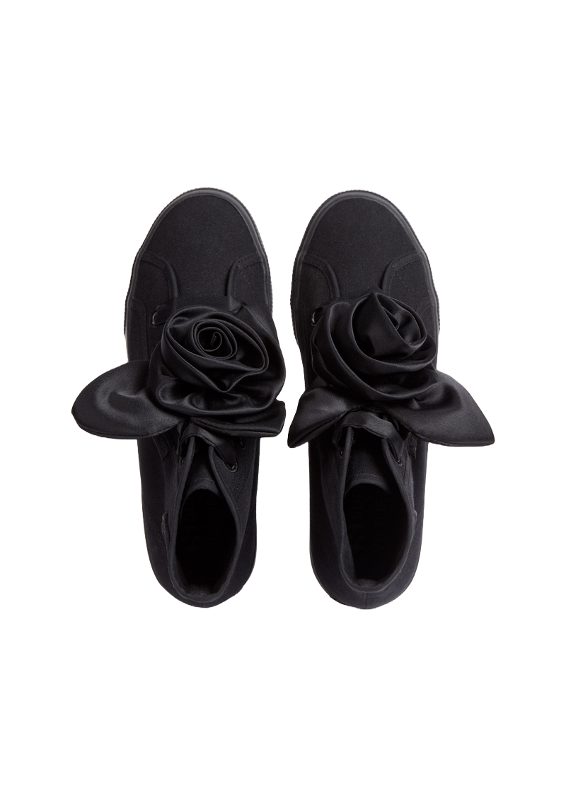 Black canvas sneakers adorned with an intricate satin rose detail, merging casual elegance with a unique floral twist.