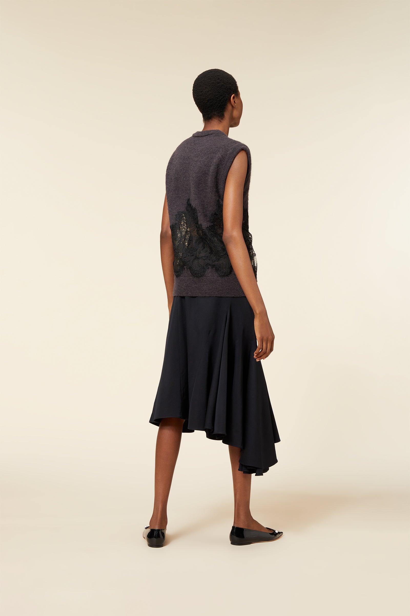 Sleeveless charcoal wool blend vest with intricate floral lace detailing, paired with an asymmetrical hem black skirt.
