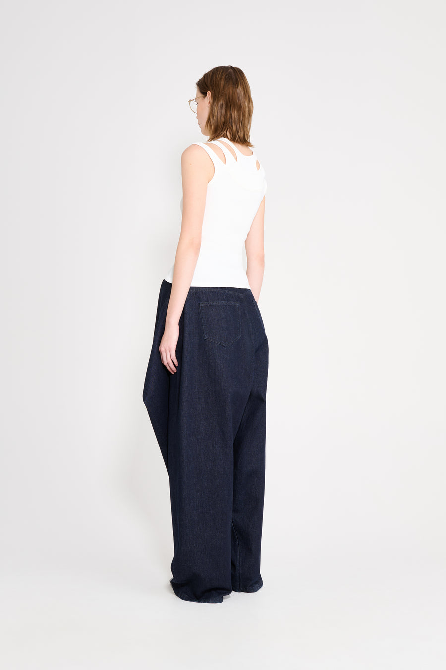 Person wearing a white sleeveless top and dark blue wide-leg pants on a white background