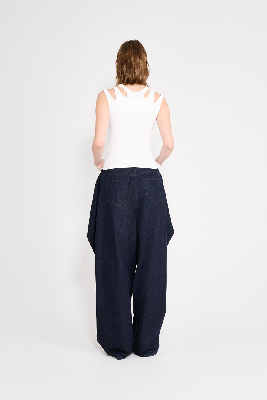 Person wearing a white sleeveless top and dark blue wide-leg pants on a white background