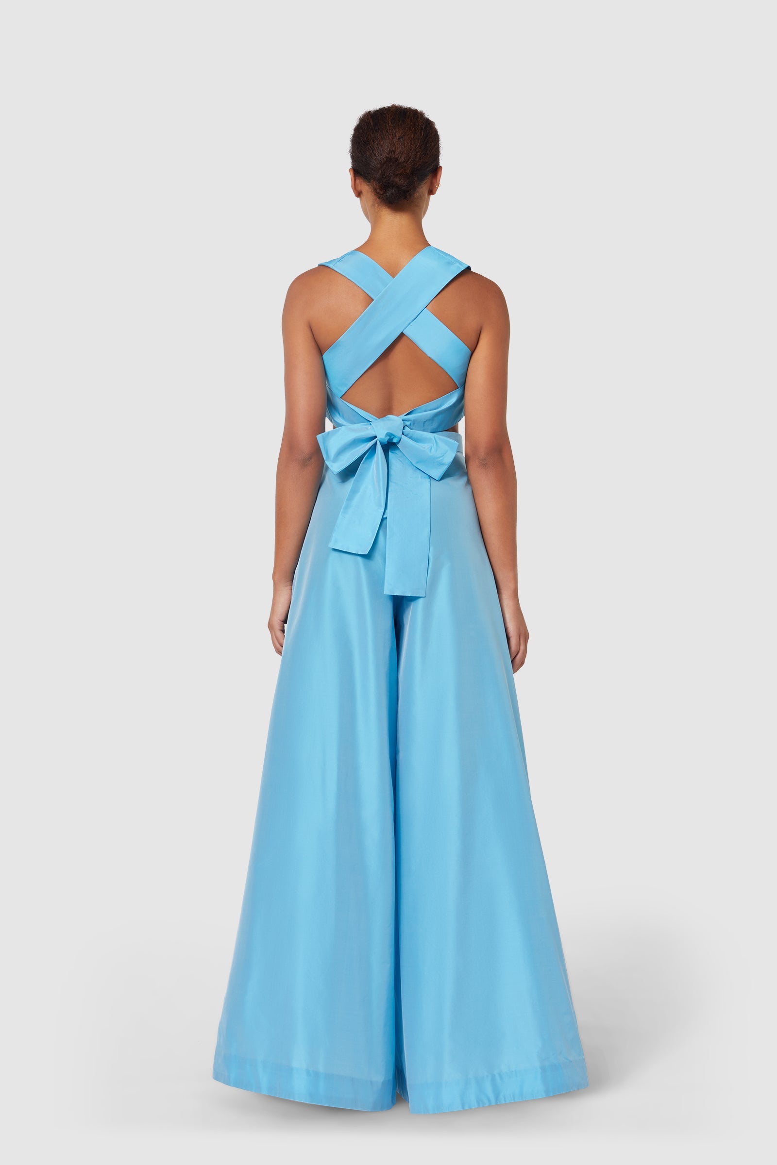 Elegant blue jumpsuit with crisscross back straps and oversized bow accent, creating a refined and sophisticated silhouette.