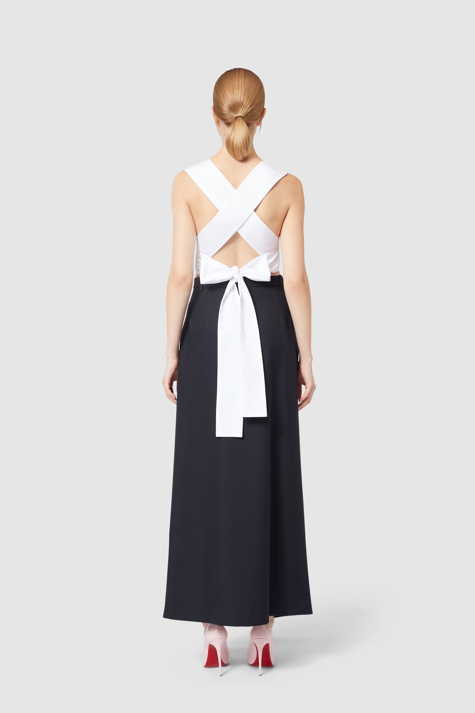 Black evening dress with crisscross white satin straps and a bow accent, elegantly styled with pink stiletto heels.