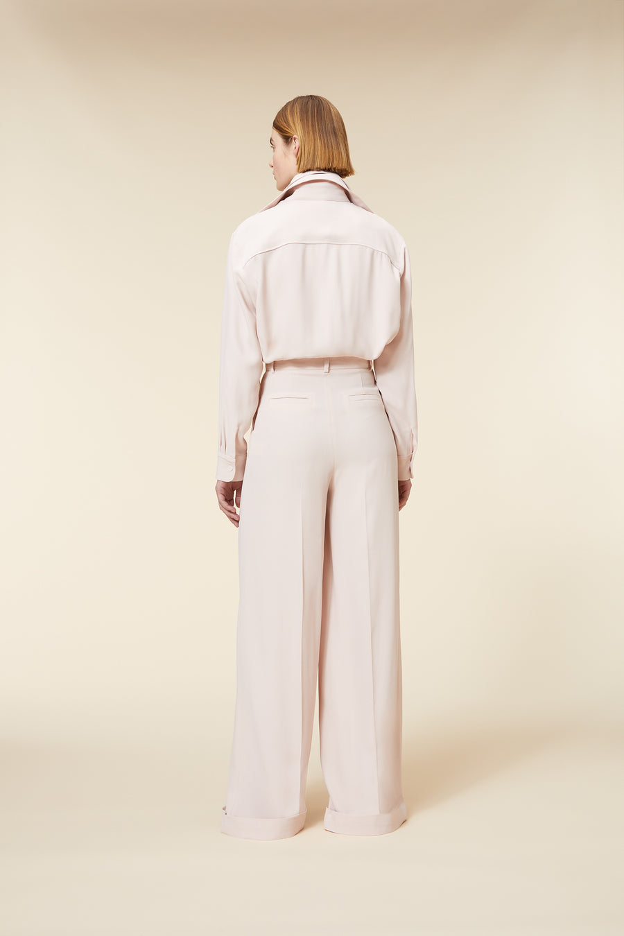 Model wearing a tailored blush pink ensemble featuring a structured button-down blouse and high-waisted wide-leg trousers.