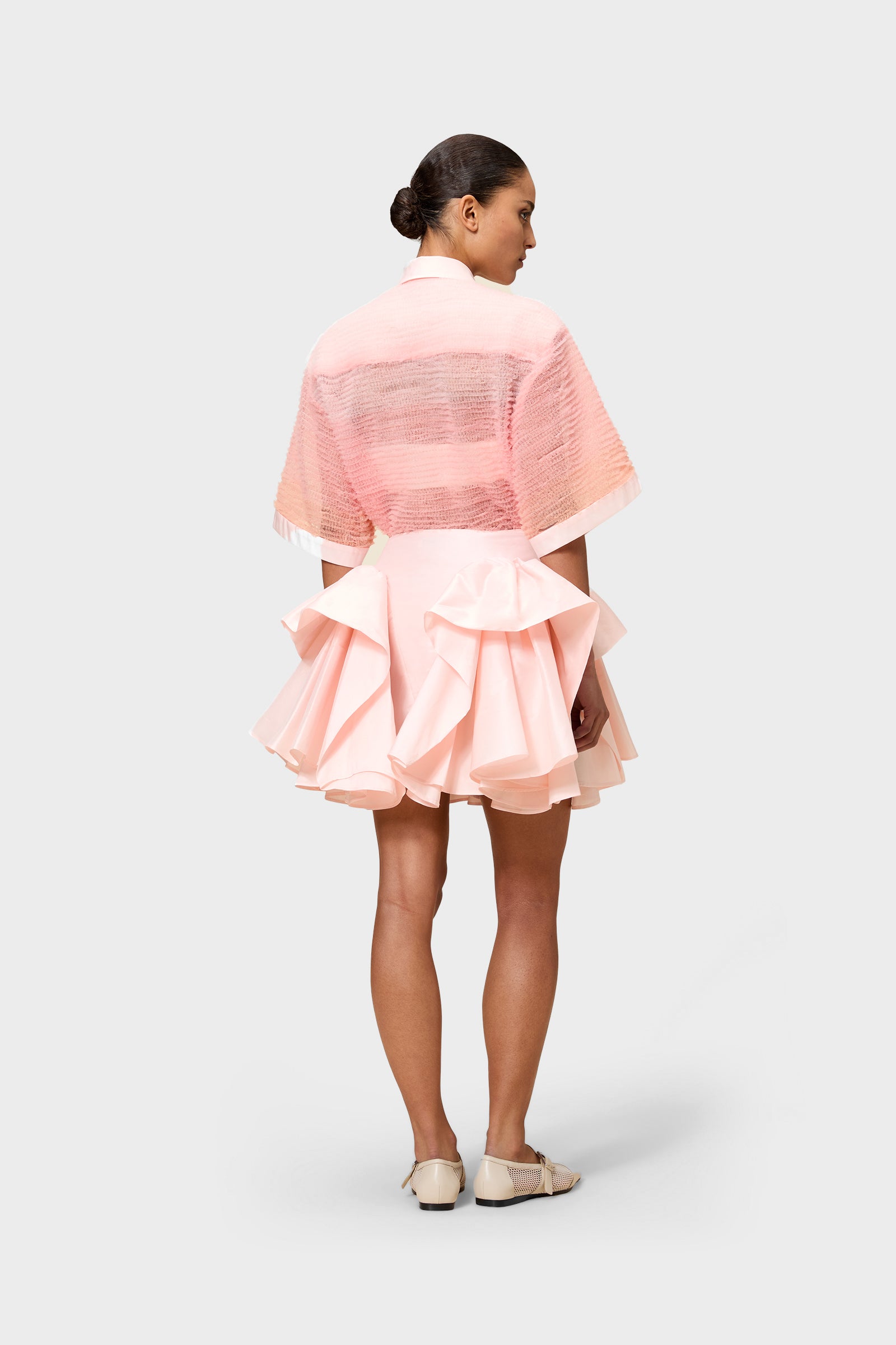 Pink tulle shirt with pink ruffled skirt on a white background worn by a model.
