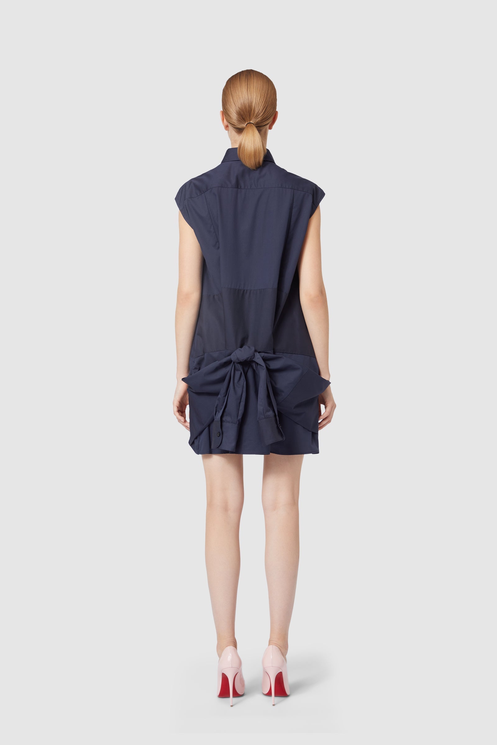 Navy blue dress with oversized back bow detail, sleeveless design, paired with elegant pale pink high heels.