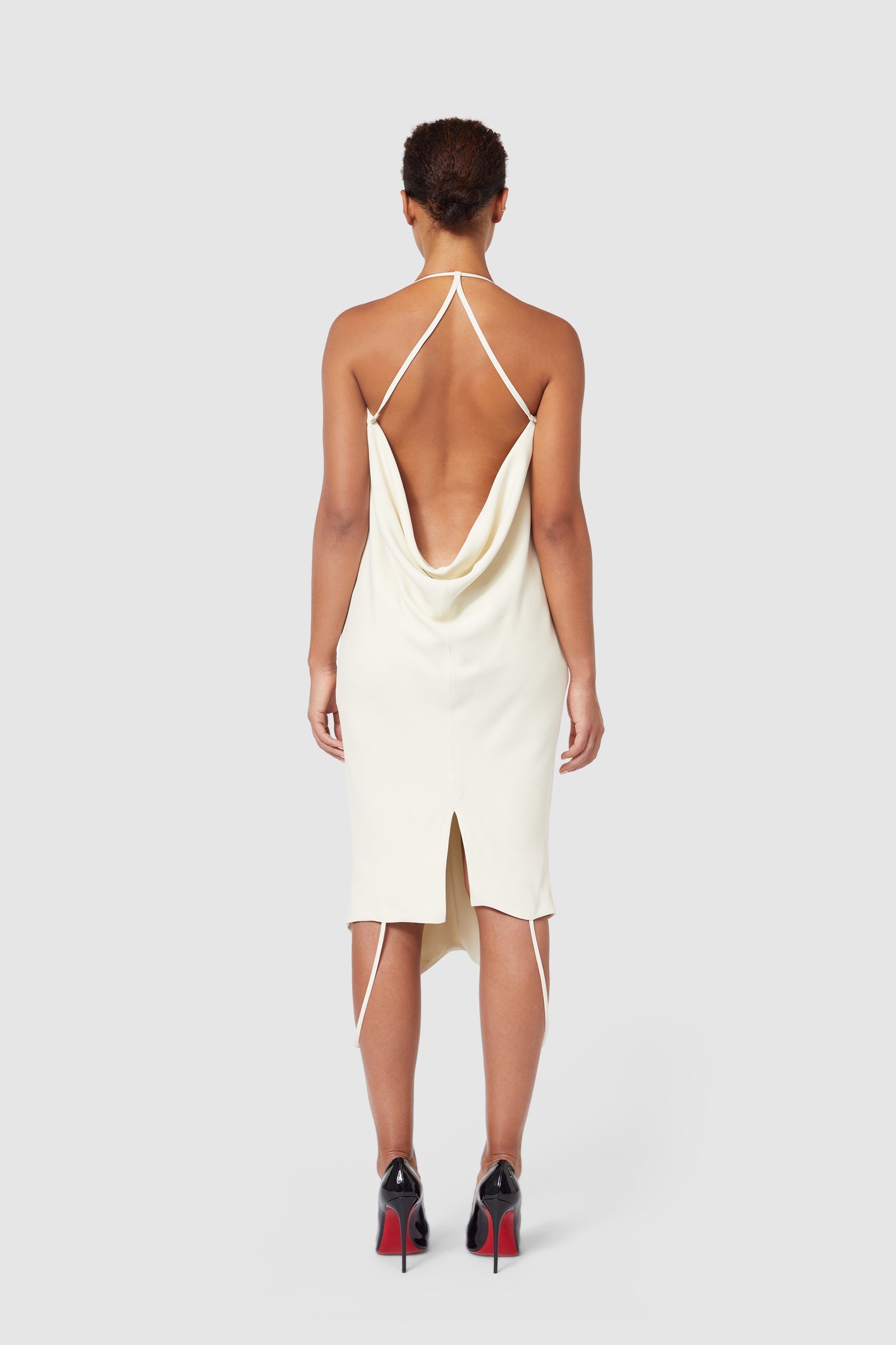 Back view of an elegant cream silk dress with a draped cowl back design, spaghetti straps, and a knee-length hem.