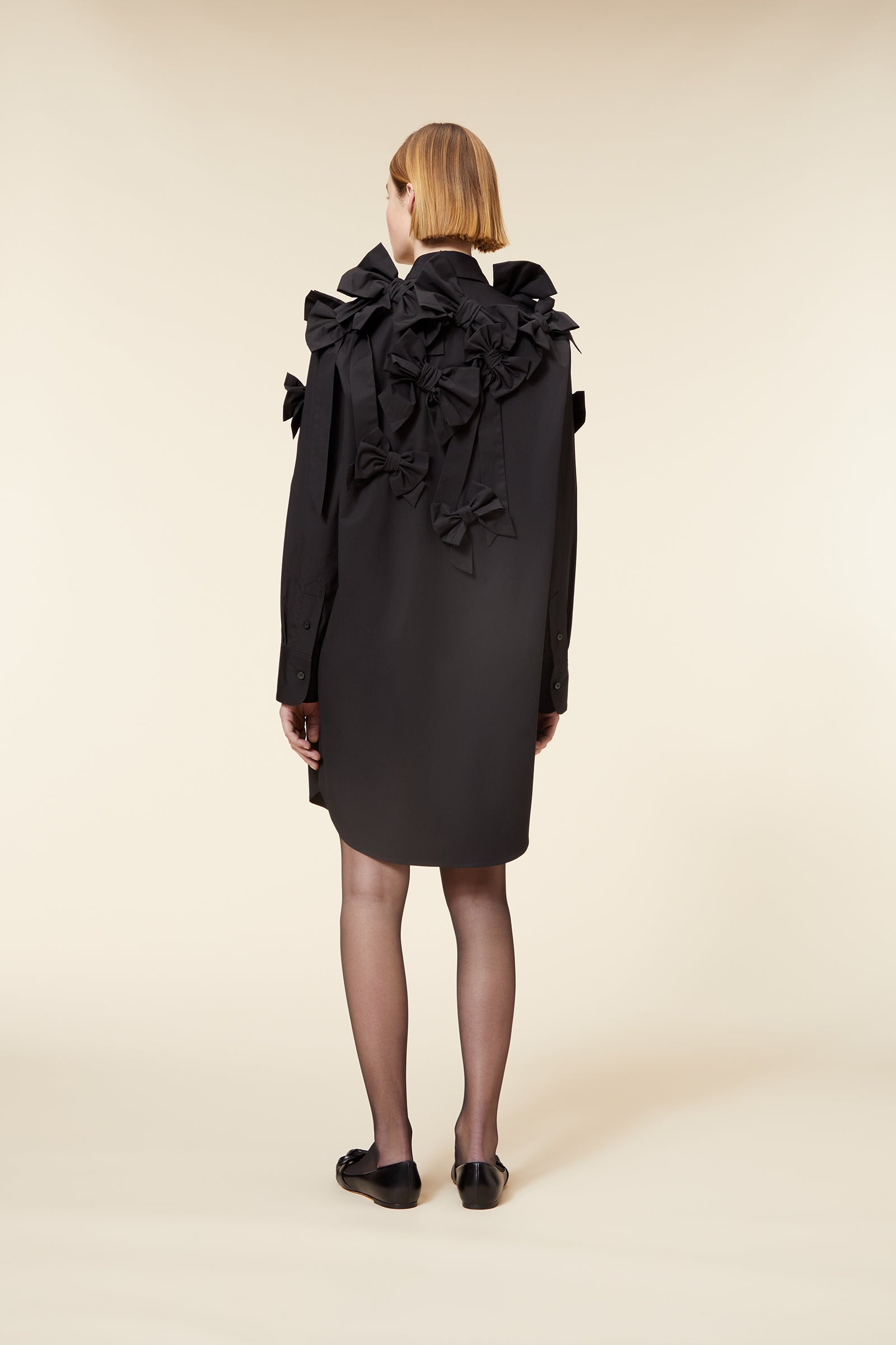 Black shirt dress with intricate ruffle and bow detailing, creating a sophisticated silhouette on a neutral background.