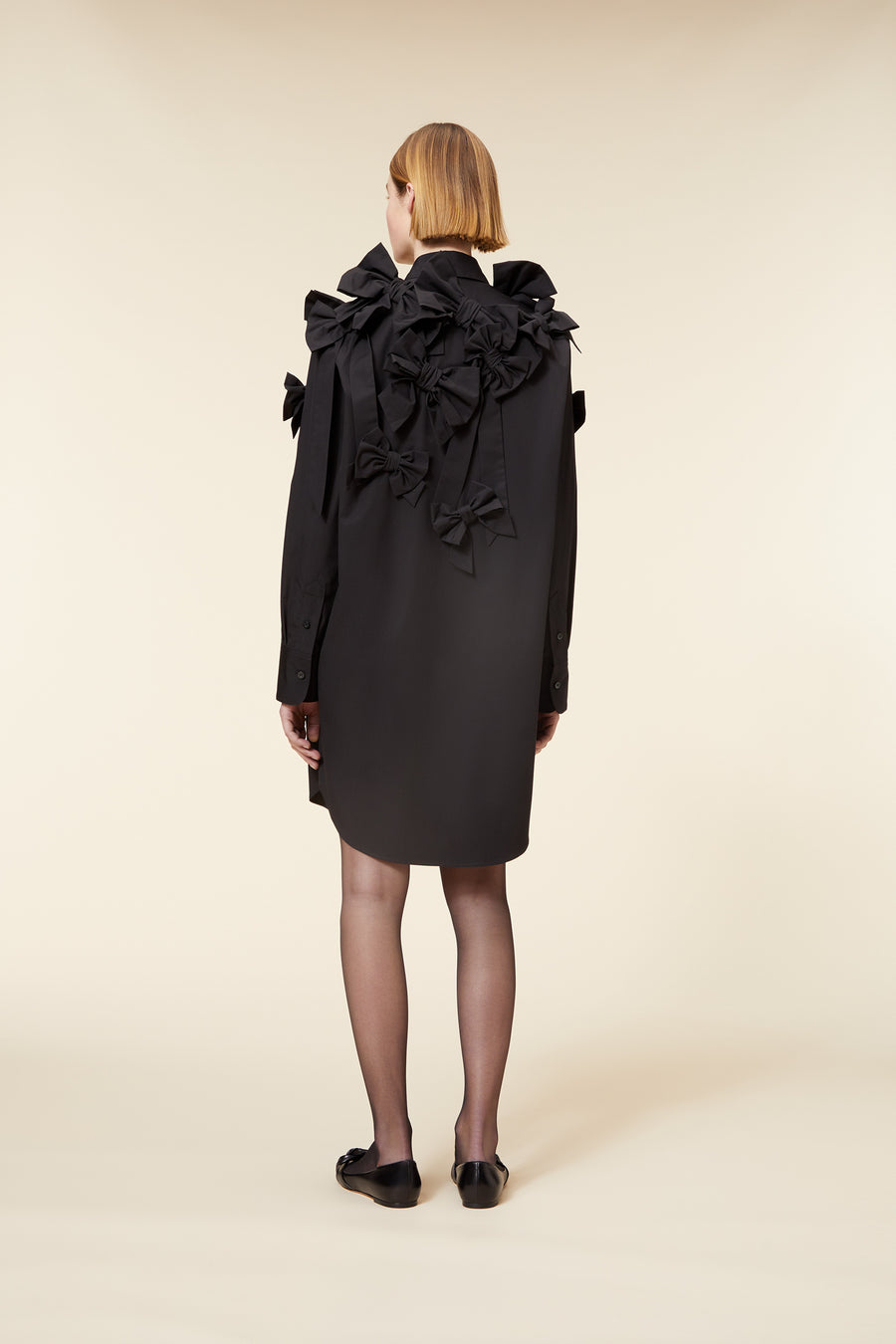 Black shirt dress with intricate ruffle and bow detailing, creating a sophisticated silhouette on a neutral background.