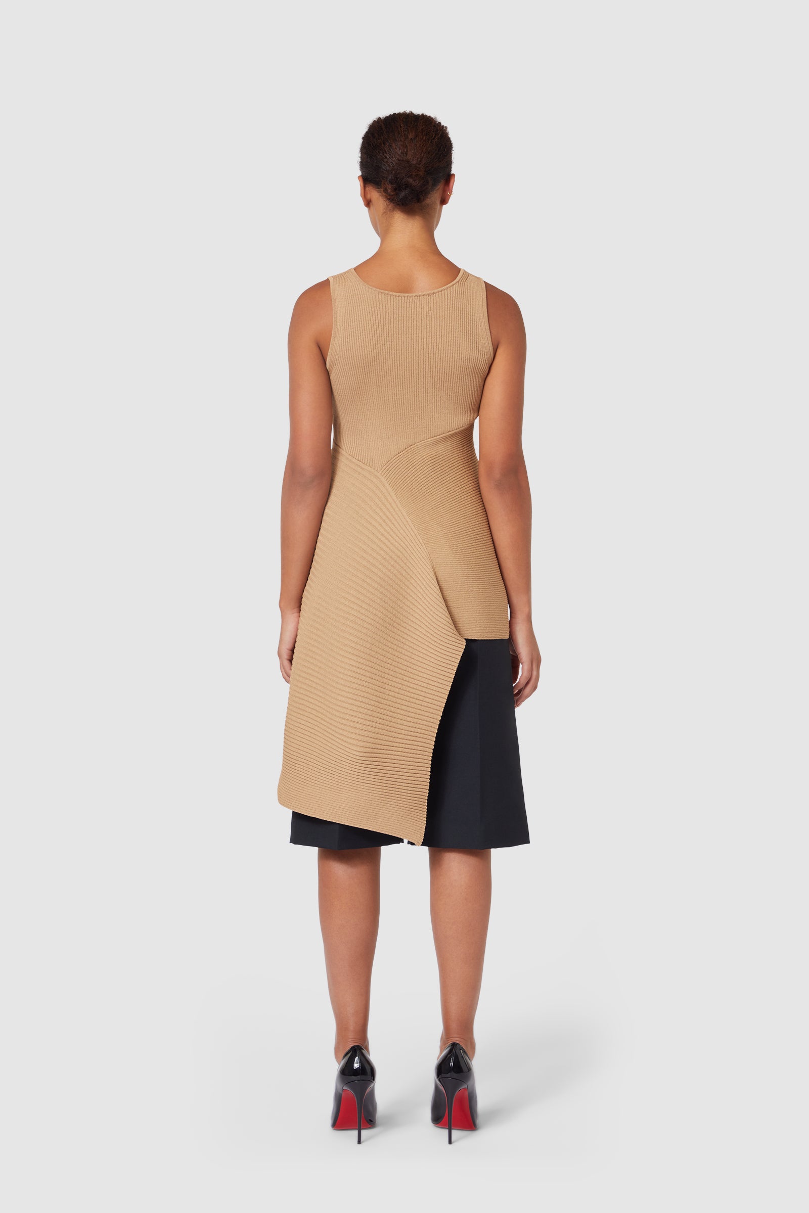 Elegant tan ribbed asymmetrical knit dress with a sleeveless design, layered over a sleek black midi pencil skirt.