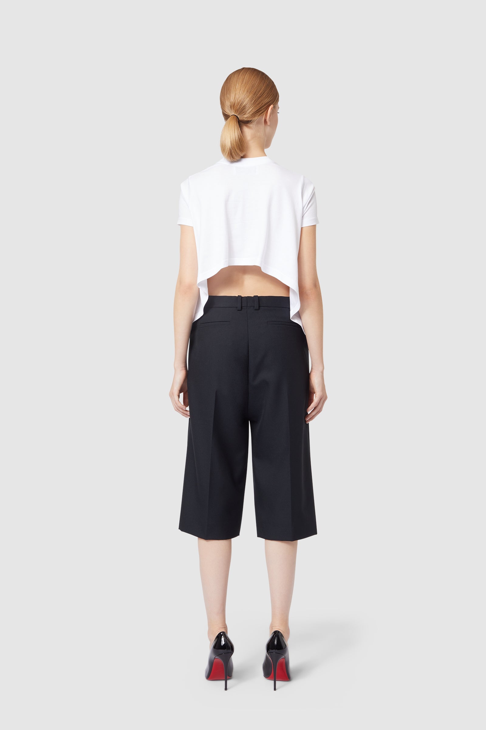 A stylish cropped white top with black high-waisted culottes, paired with sleek black heels featuring red soles.