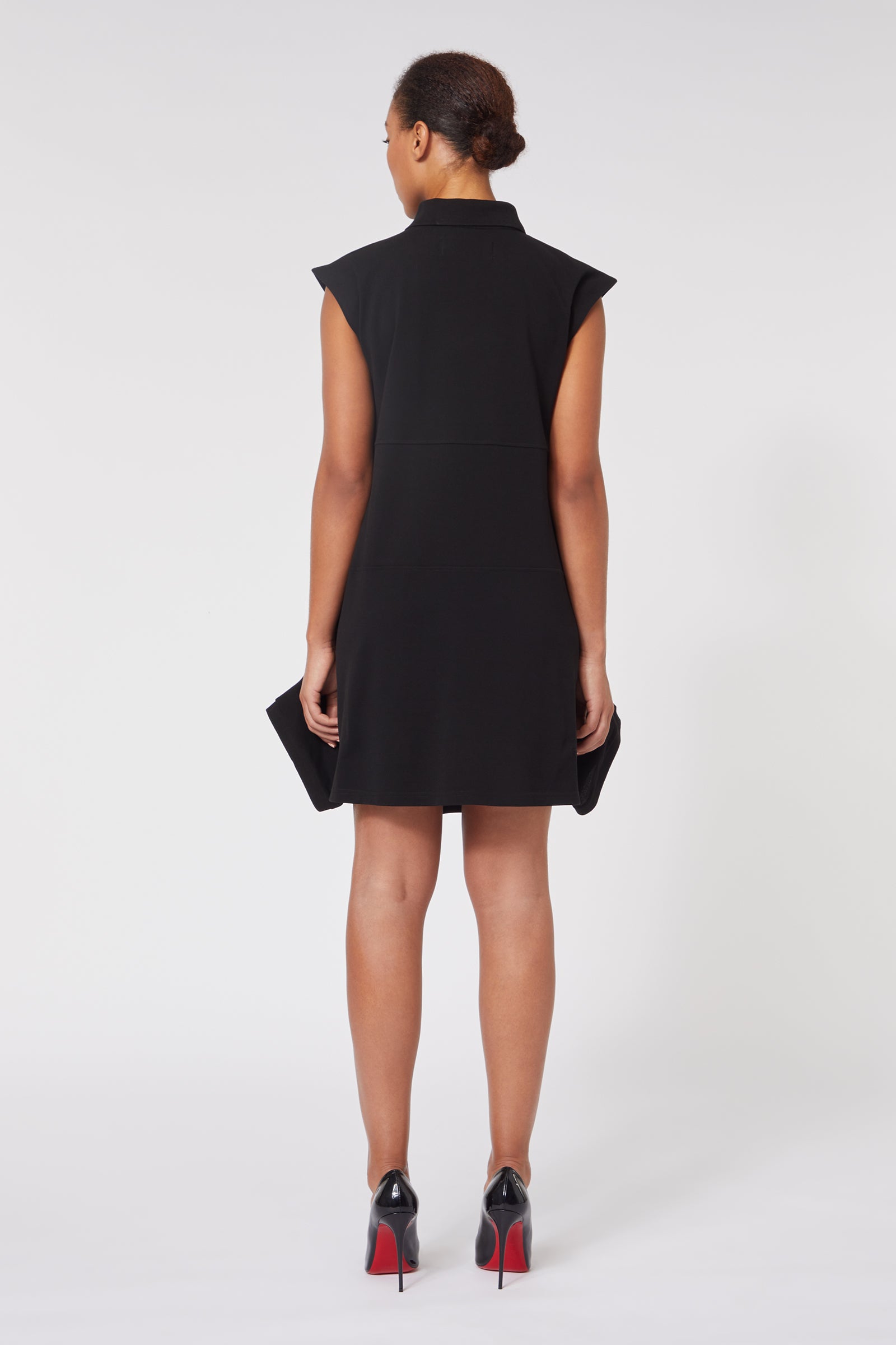 Sleeveless black dress with structured shoulders and a high neckline, worn with chic black high heels with red soles.