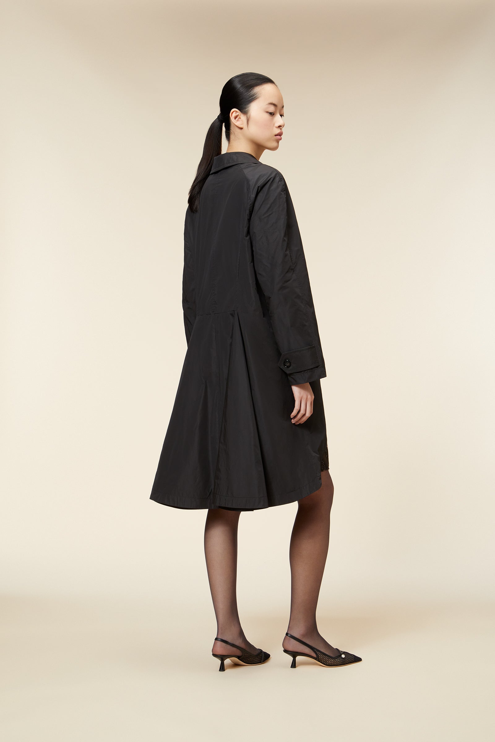 A stylish black trench coat with a classic collar and elegant back pleats, paired with chic slingback heels.