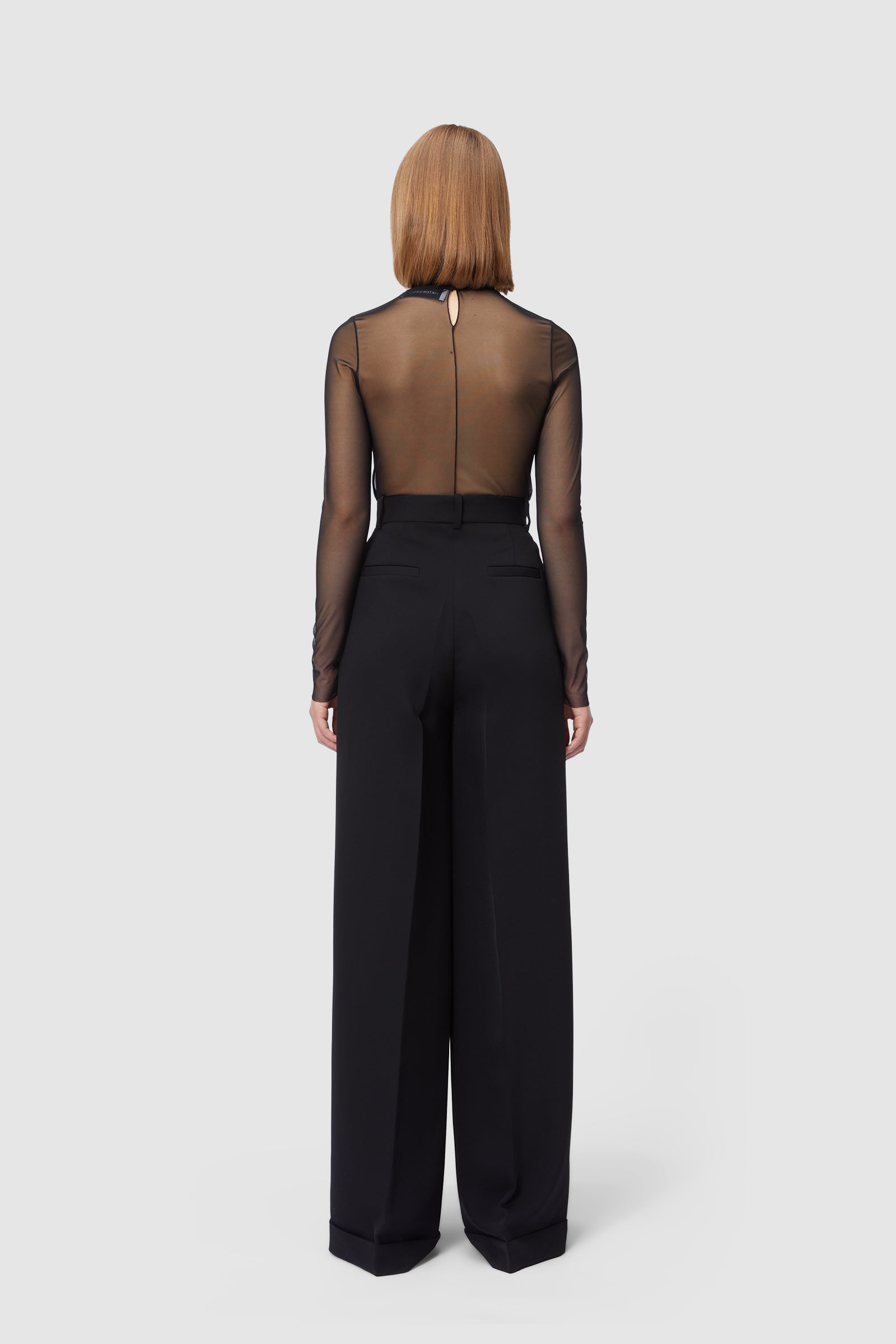 Sheer black mesh top paired with elegant high-waisted wide-leg trousers, showcasing modern and sophisticated fashion style.