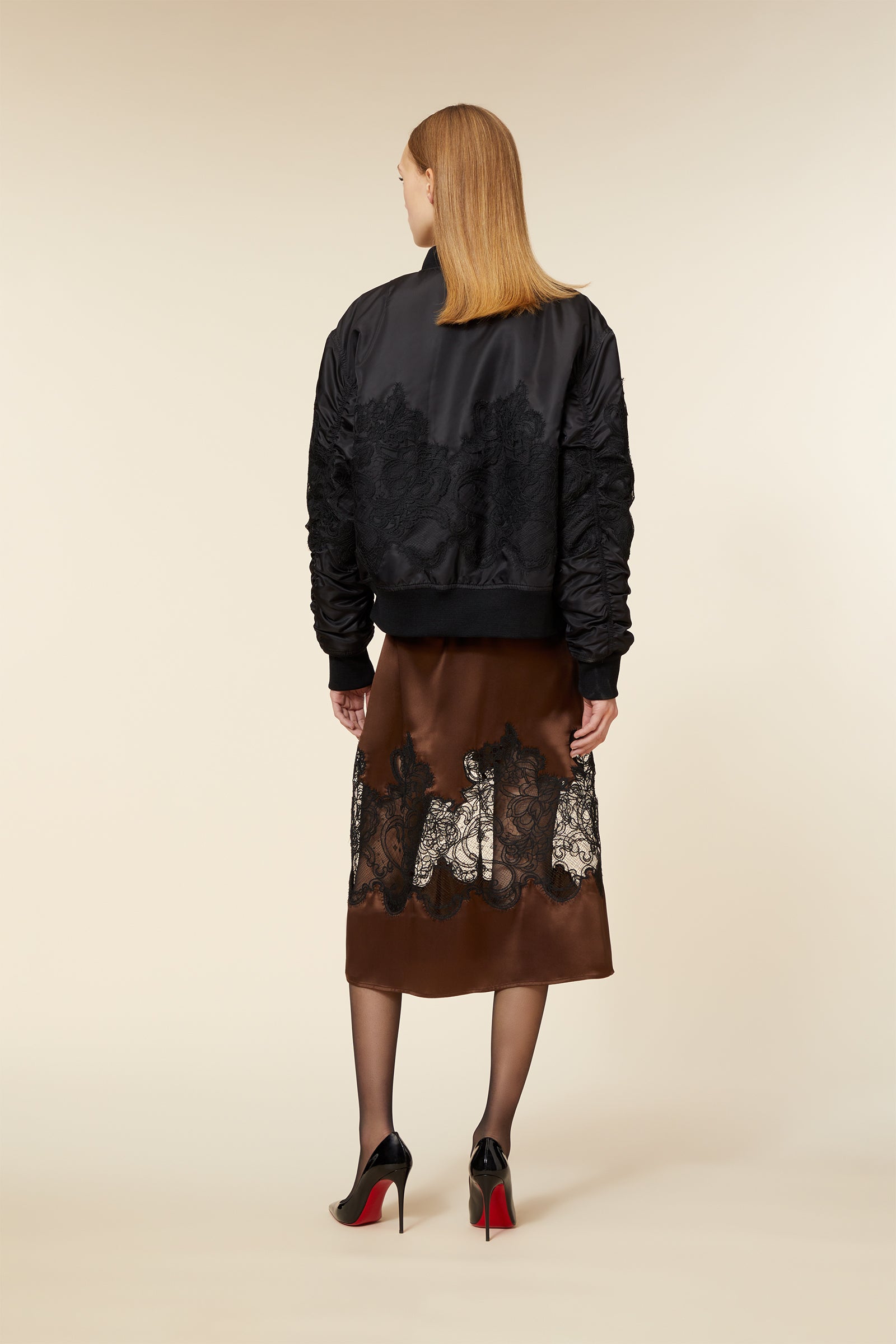 A black satin bomber jacket with intricate lace detailing paired with a brown silk skirt featuring black lace patterns.