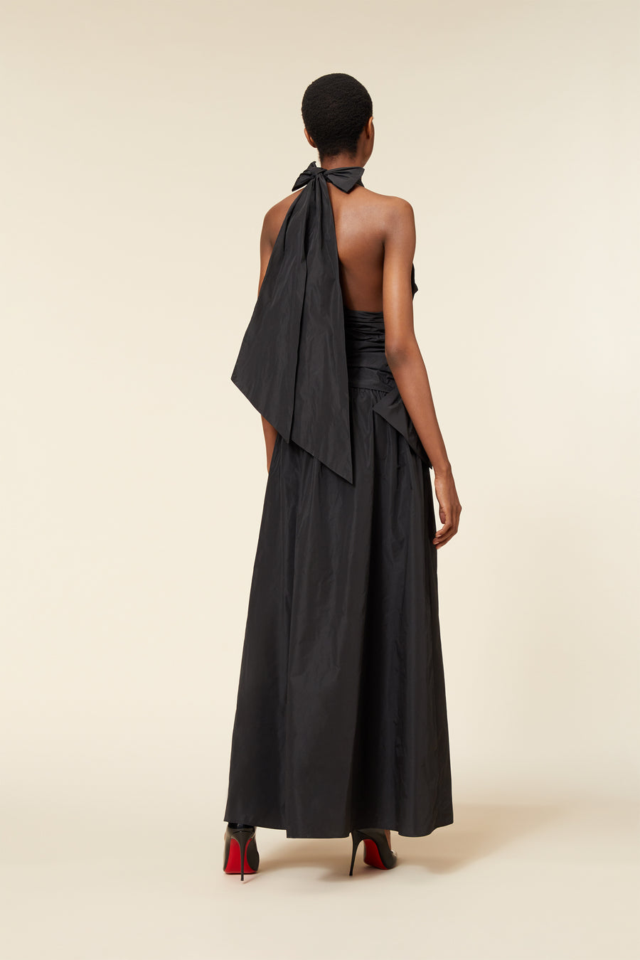 Elegant long black dress with large bows and halter neckline, highlighting a chic, sophisticated fashion style.