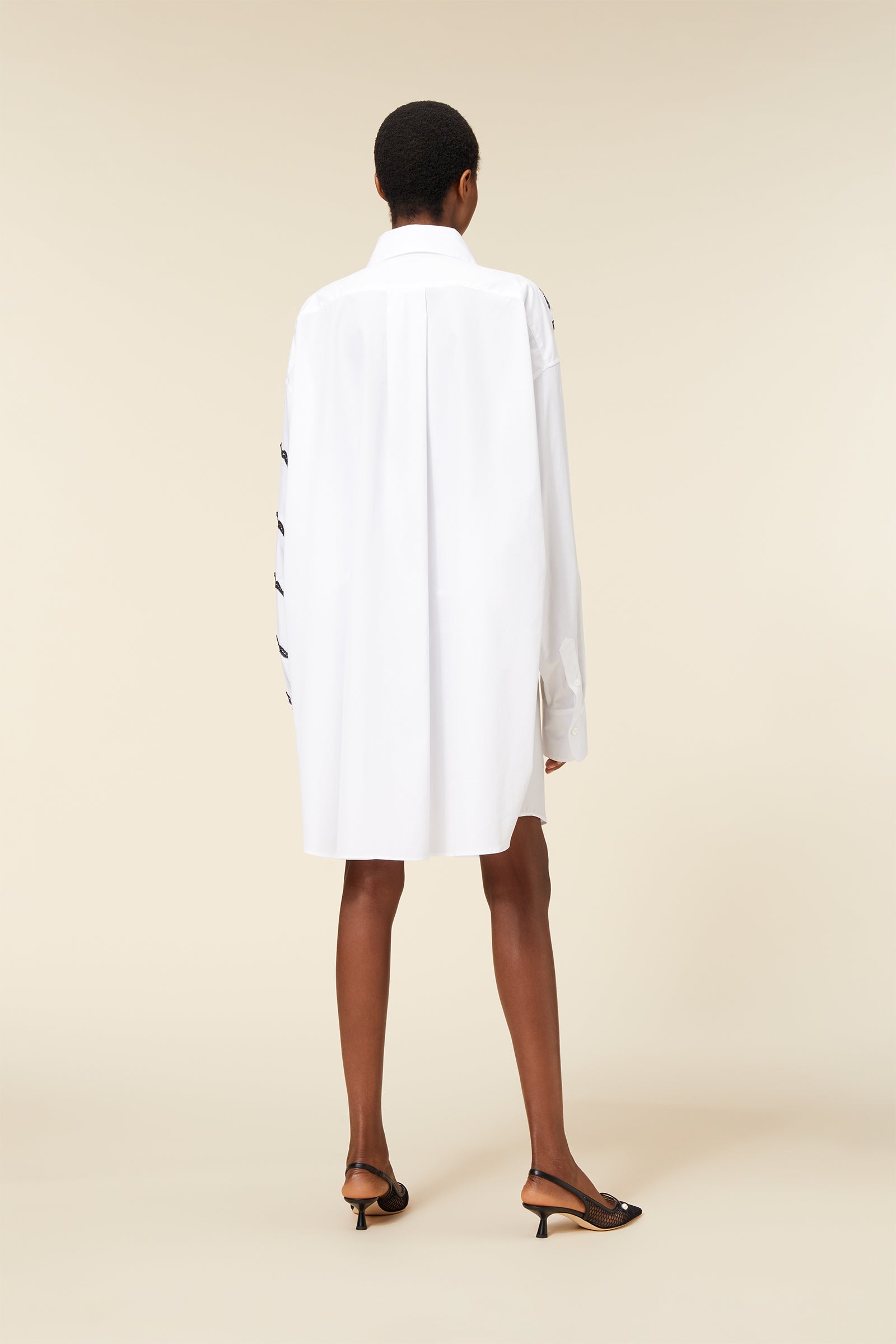 Elegant long white shirt dress featuring minimalist design, loose fit, button-up cuffs, and black ribbon details on sleeves.