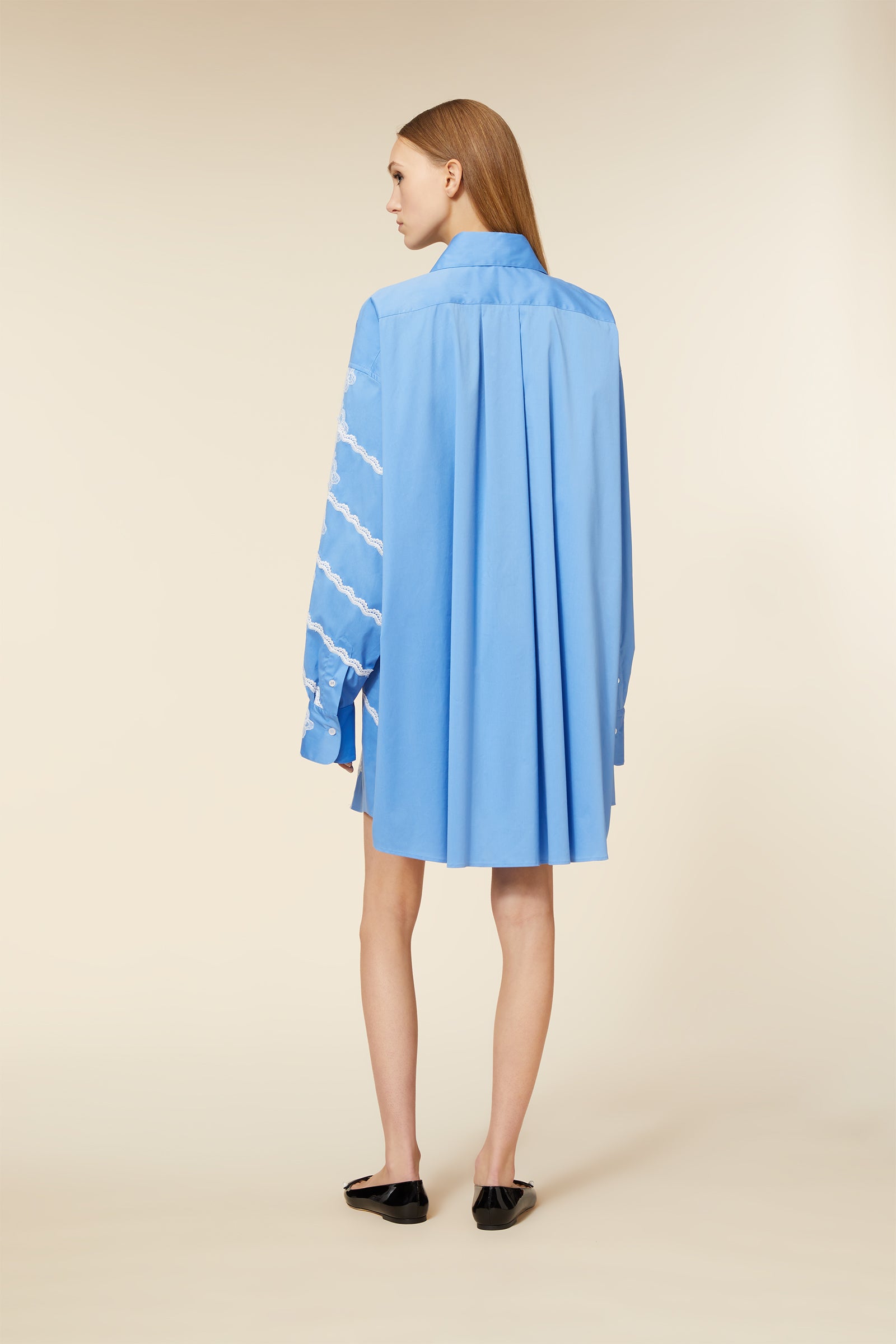 Oversized blue shirt dress with pleated back and lace details on sleeves, paired with black patent loafers.
