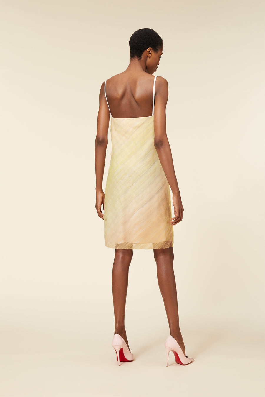 Model wearing a light pastel-colored, sleeveless dress with thin straps and subtle geometric patterns.
