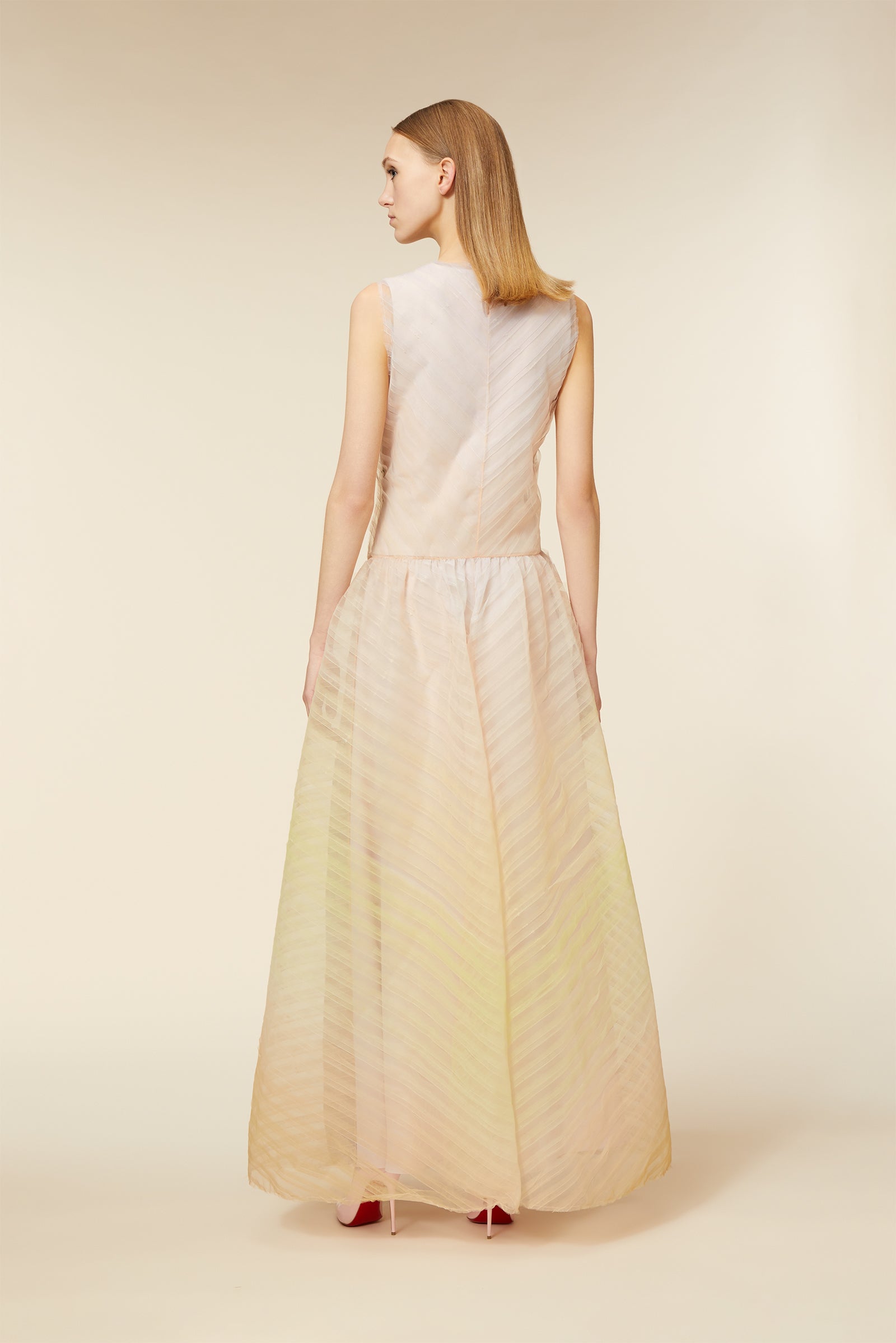 Elegant long beige dress with sheer stripes and sleeveless design, viewed from the back against a neutral background.