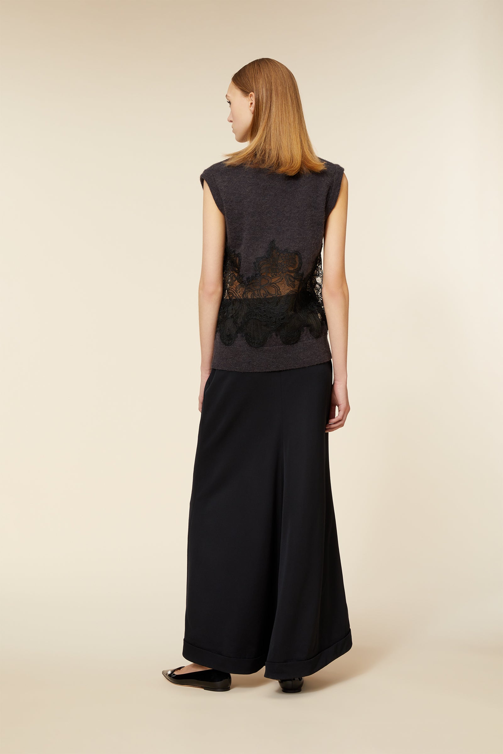 A sleeveless charcoal top with intricate black lace detailing, paired with flowing black wide-leg trousers.