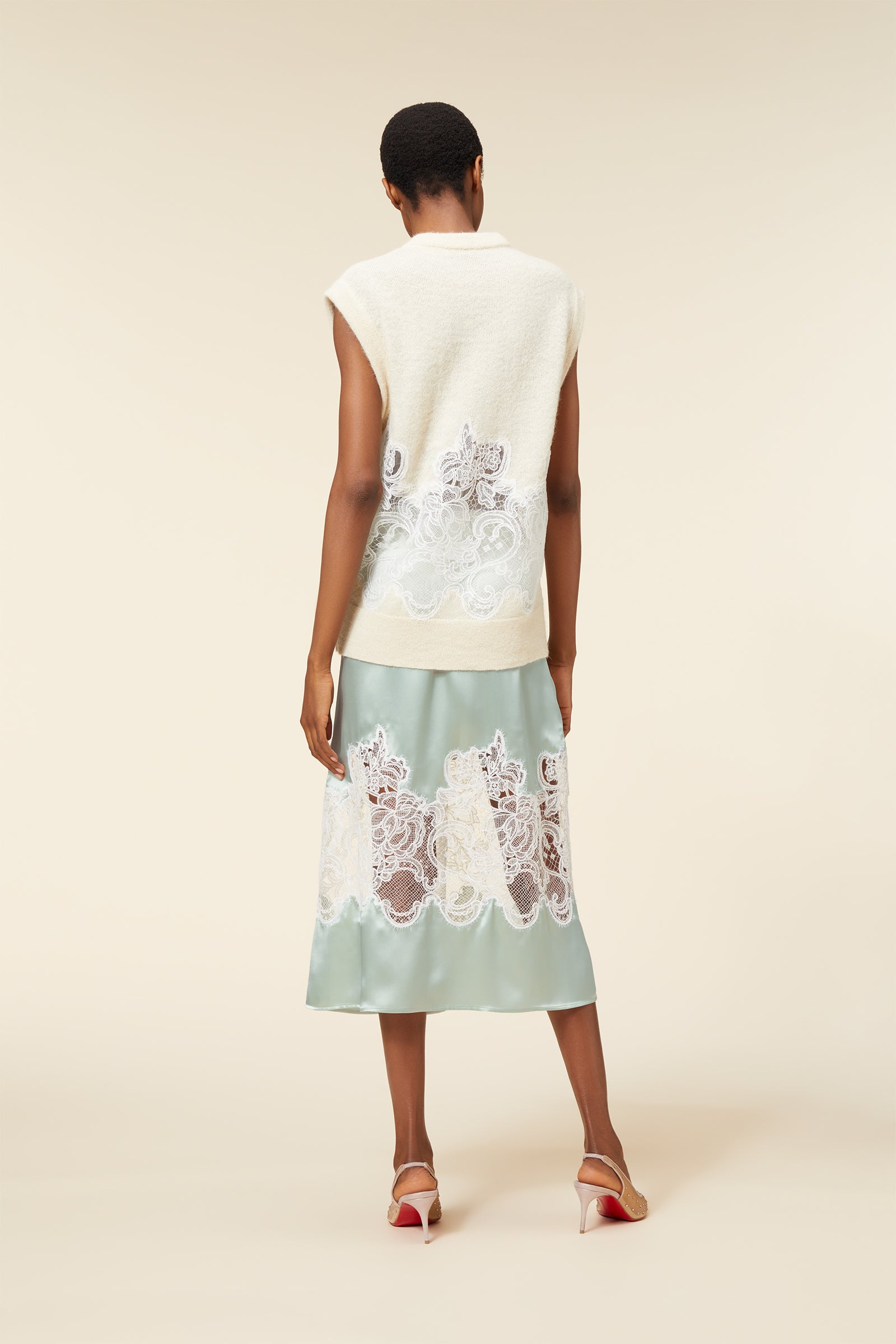 Elegant sleeveless vest with intricate lace detailing over a silky, pastel green skirt, complemented by chic high-heeled shoes.