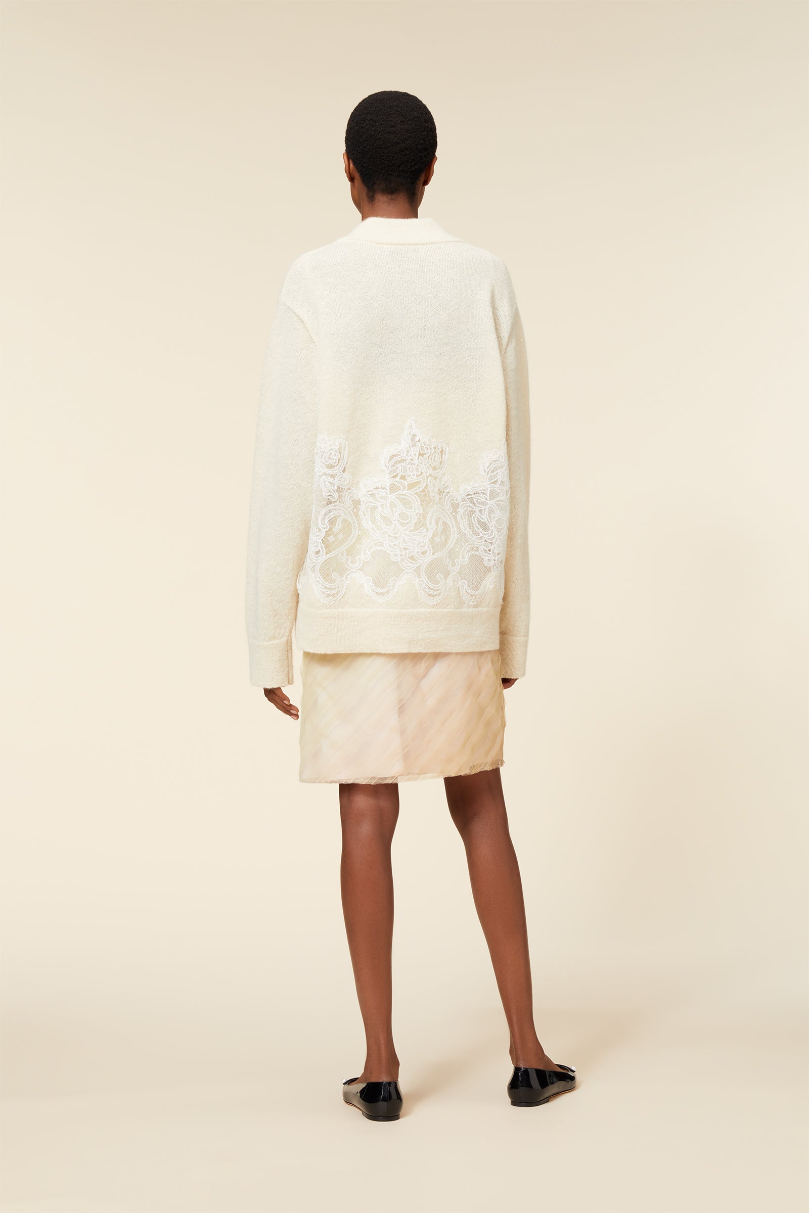 Elegant cream sweater with intricate lace embroidery over sheer layer, paired with a subtle striped beige skirt.