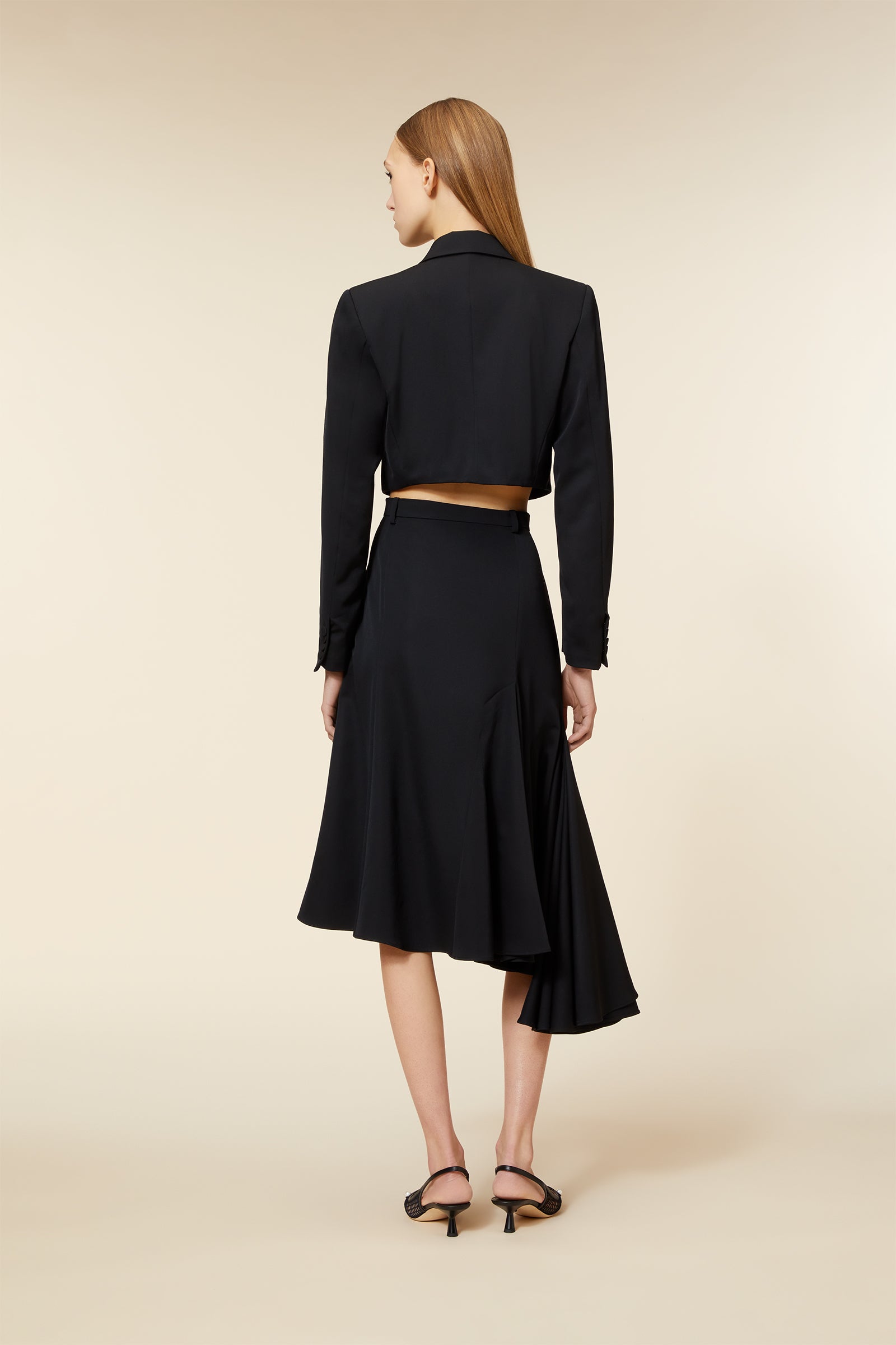 Black tailored blazer and midi skirt set with asymmetrical hem, crafted in smooth fabric, featuring a cropped fit and long sleeves.