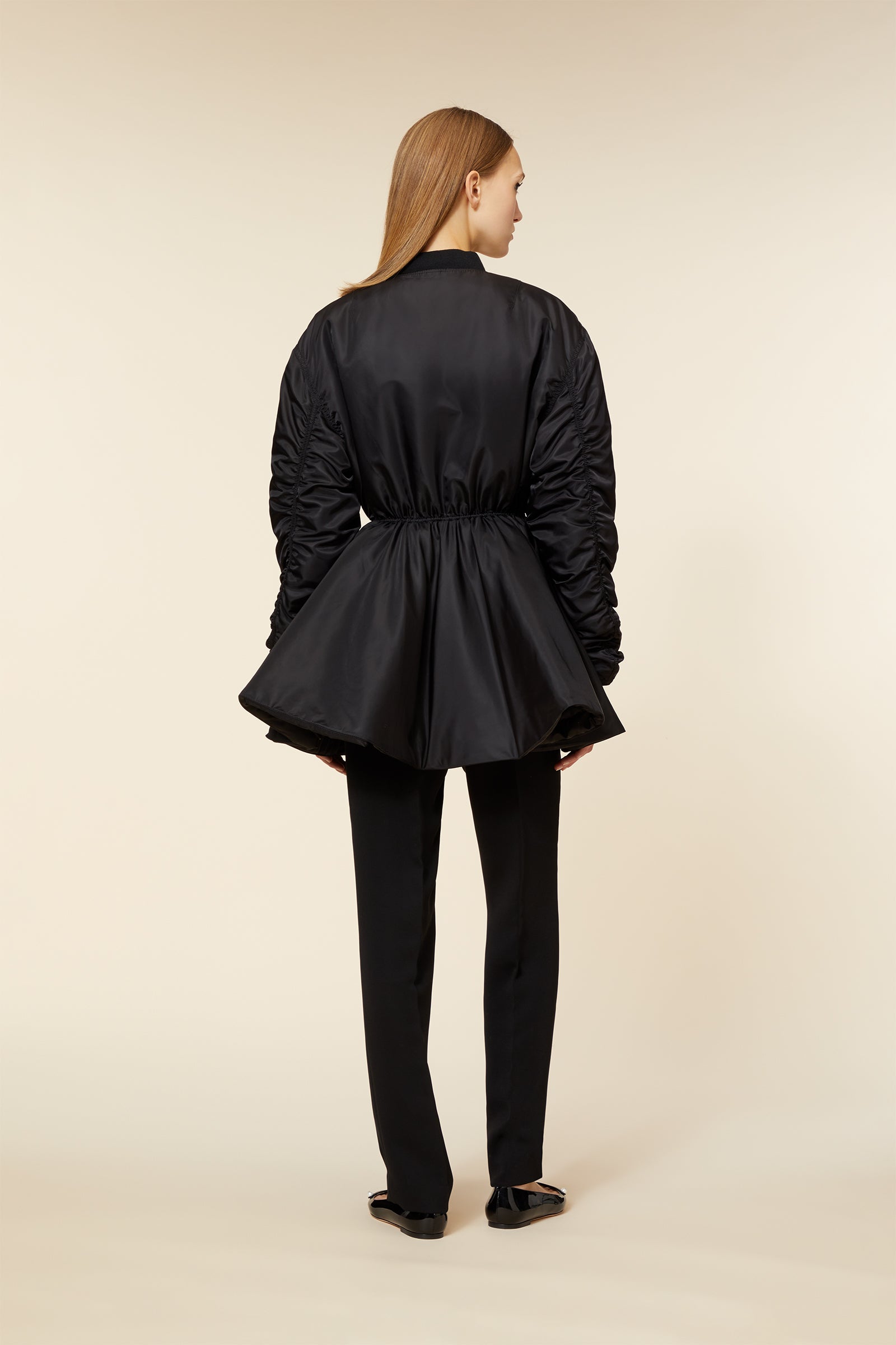 Black satin jacket with ruched sleeves and a cinched waist, paired with tailored black trousers and elegant flats.