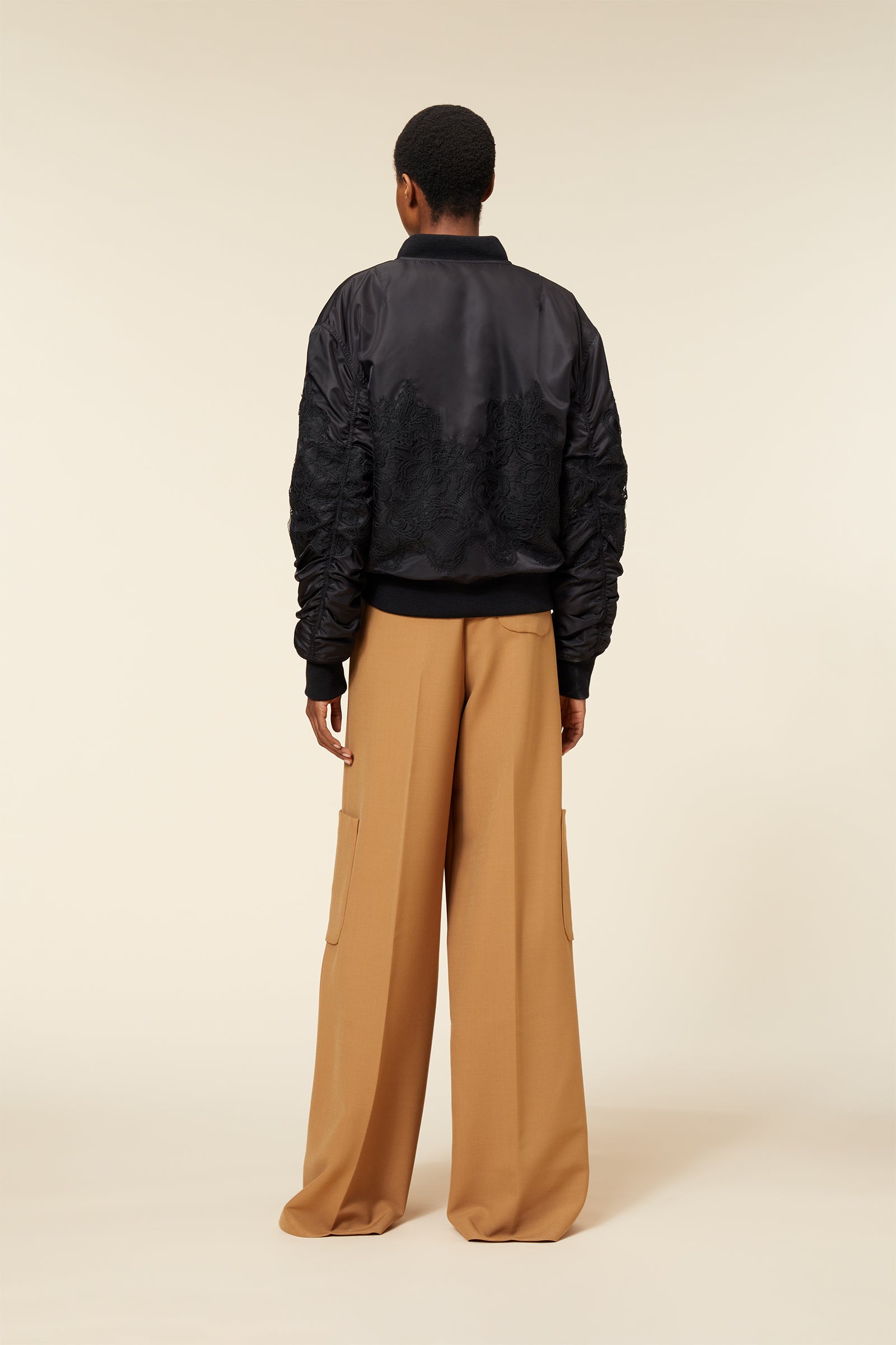 Black satin bomber jacket with intricate lace embroidery paired with wide-leg tan cargo pants showcasing sleek fashion.